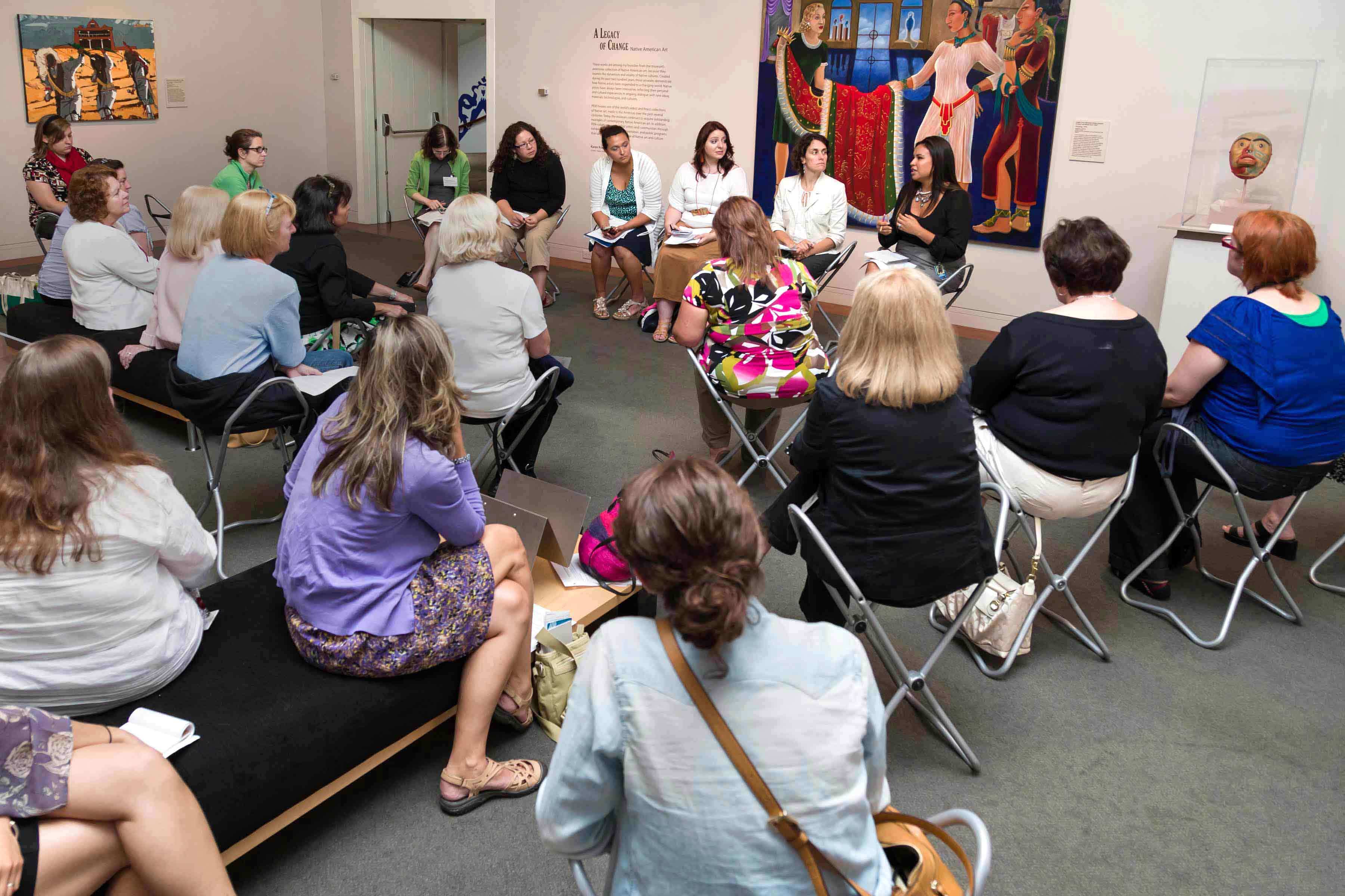 A group of women sitting in a chair circle and listening to a talk by a woman in the front of the room