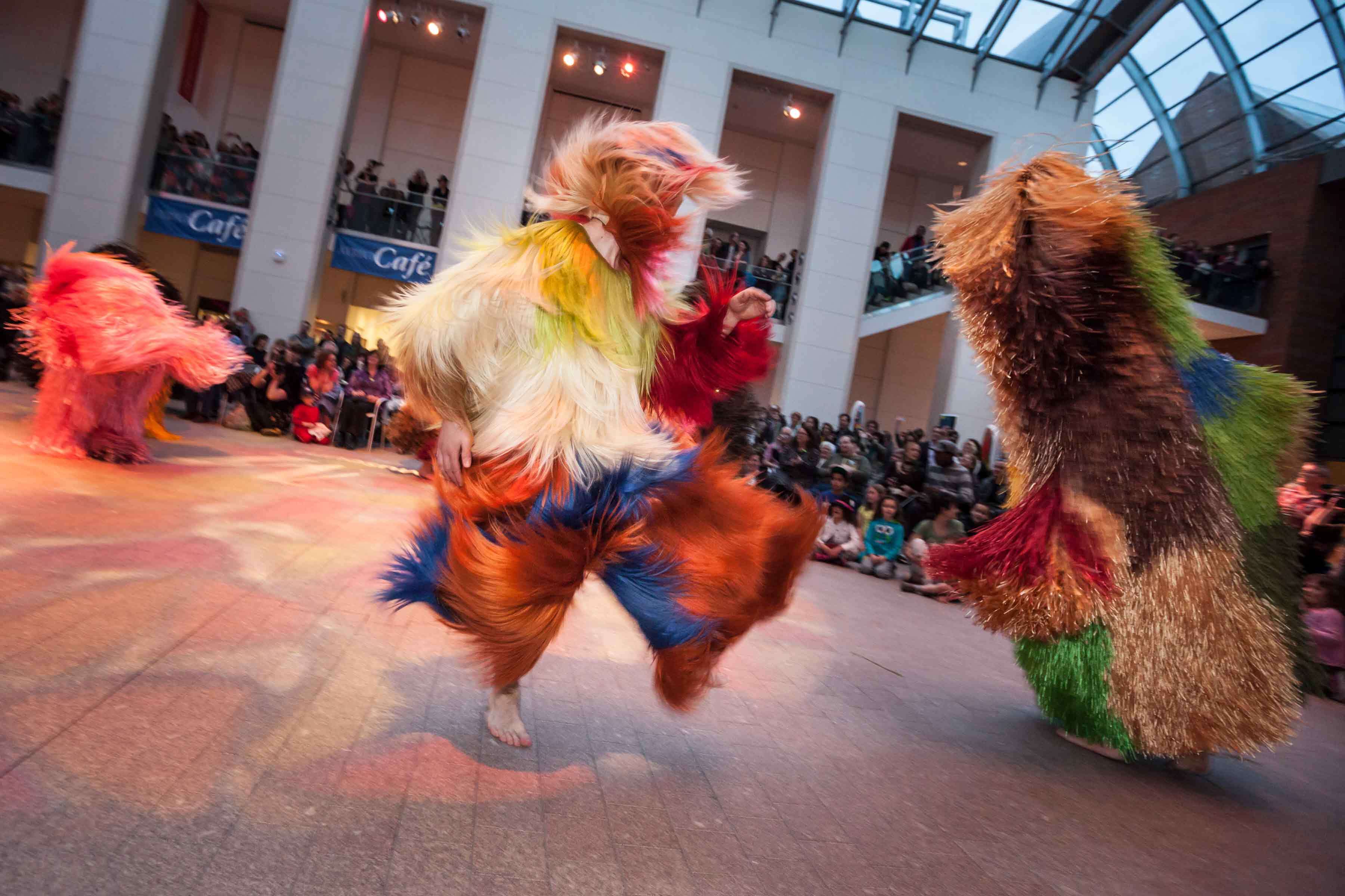 Nick Cave Soundsuits dancing in the Atrium with a seated crowd watching on.