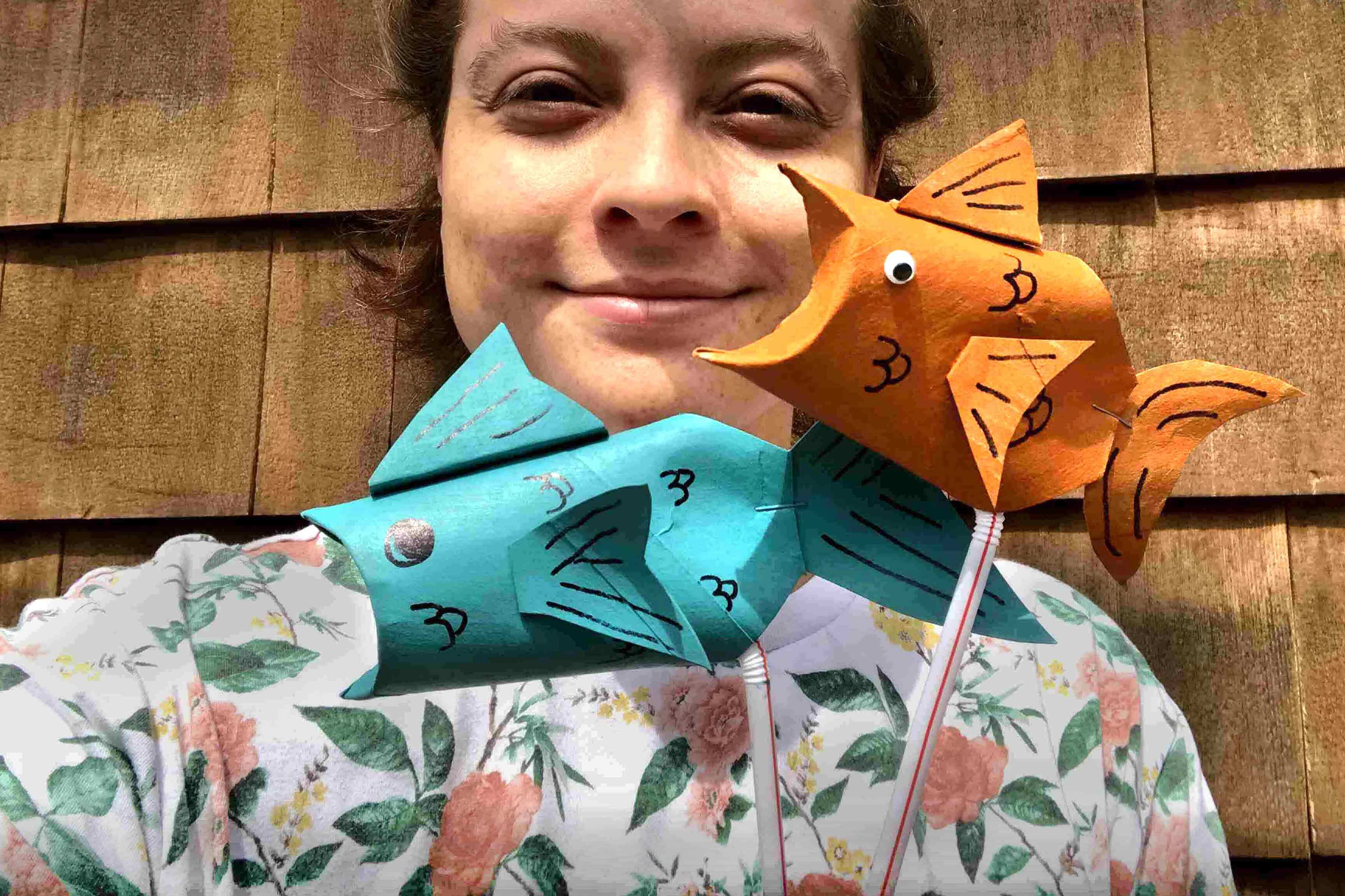 A girl is holding two handmade paper fish puppets