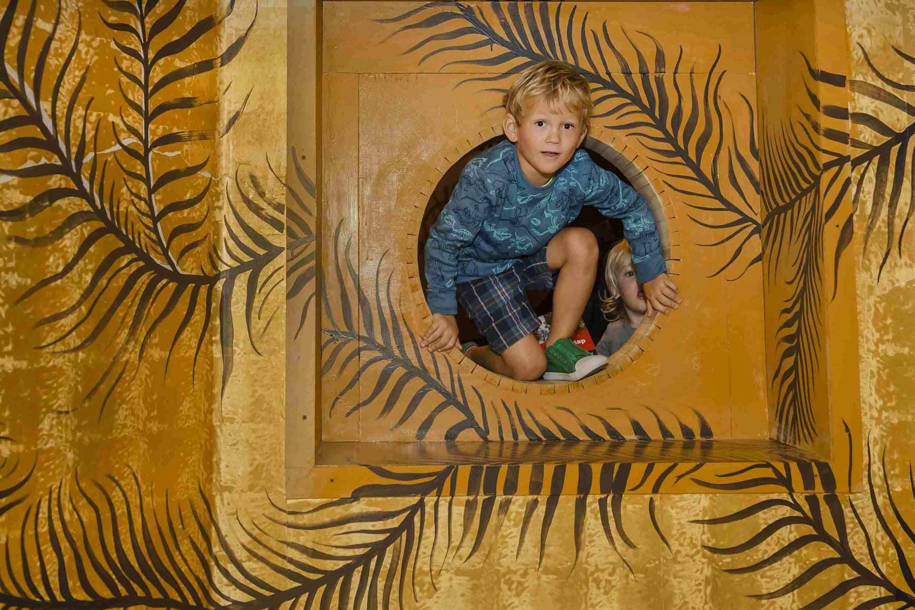 Visit Families A young boy climbs through a portal of a yellow wall with black vines painted on it