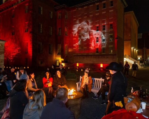 Nighttime gathering with attendees seated in front of a red-lit brick building showing a projected image from the film Nosferatu