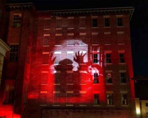 Exterior of a brick building at night with a light projection of the film Nosferatu