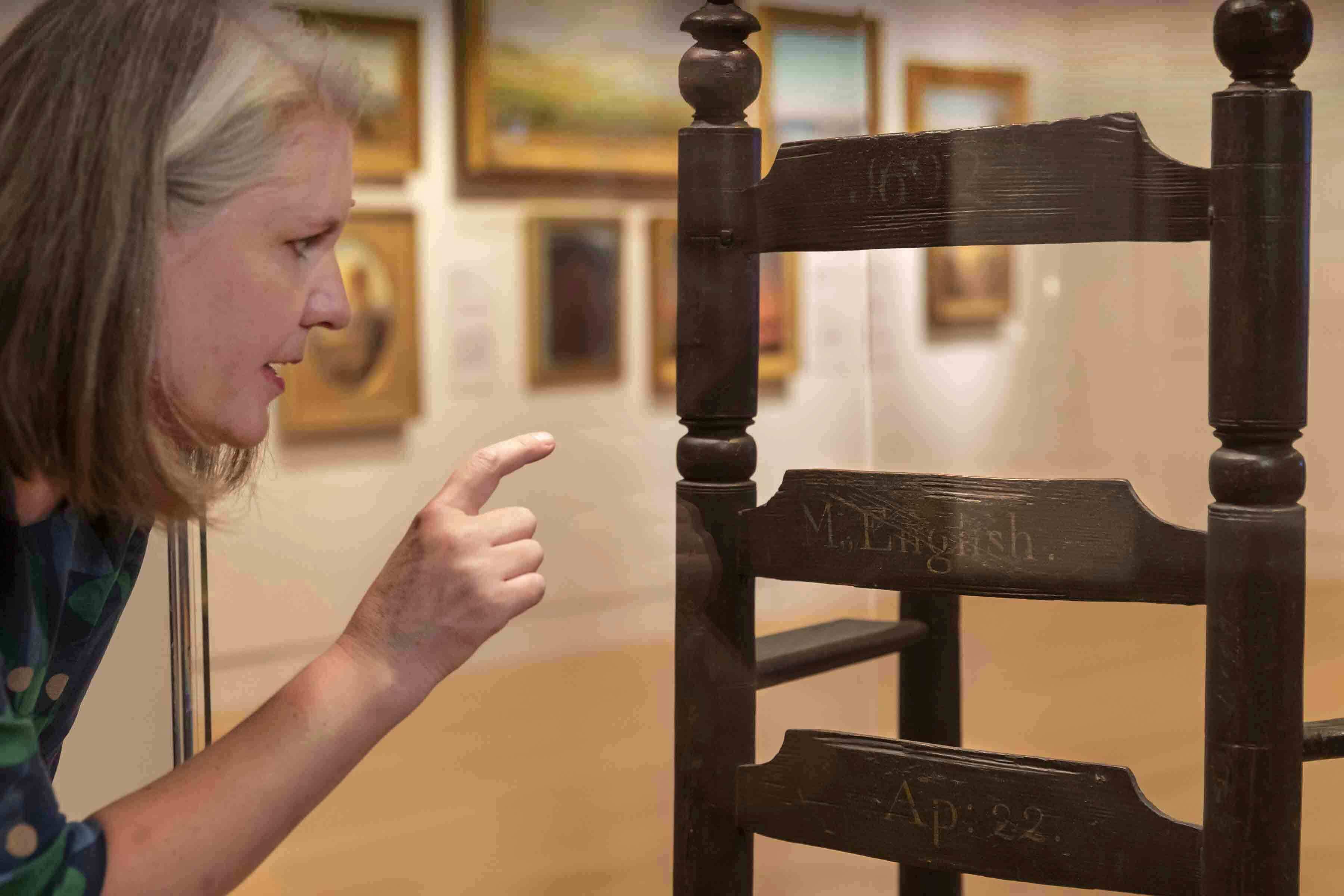 PEM Associate Curator Sarah Chasse points out details on the back of a chair owned by Philip and Mary English who were able to escape the trials and come back to Salem after it was all over. Photo by Kathy Tarantola/PEM.
