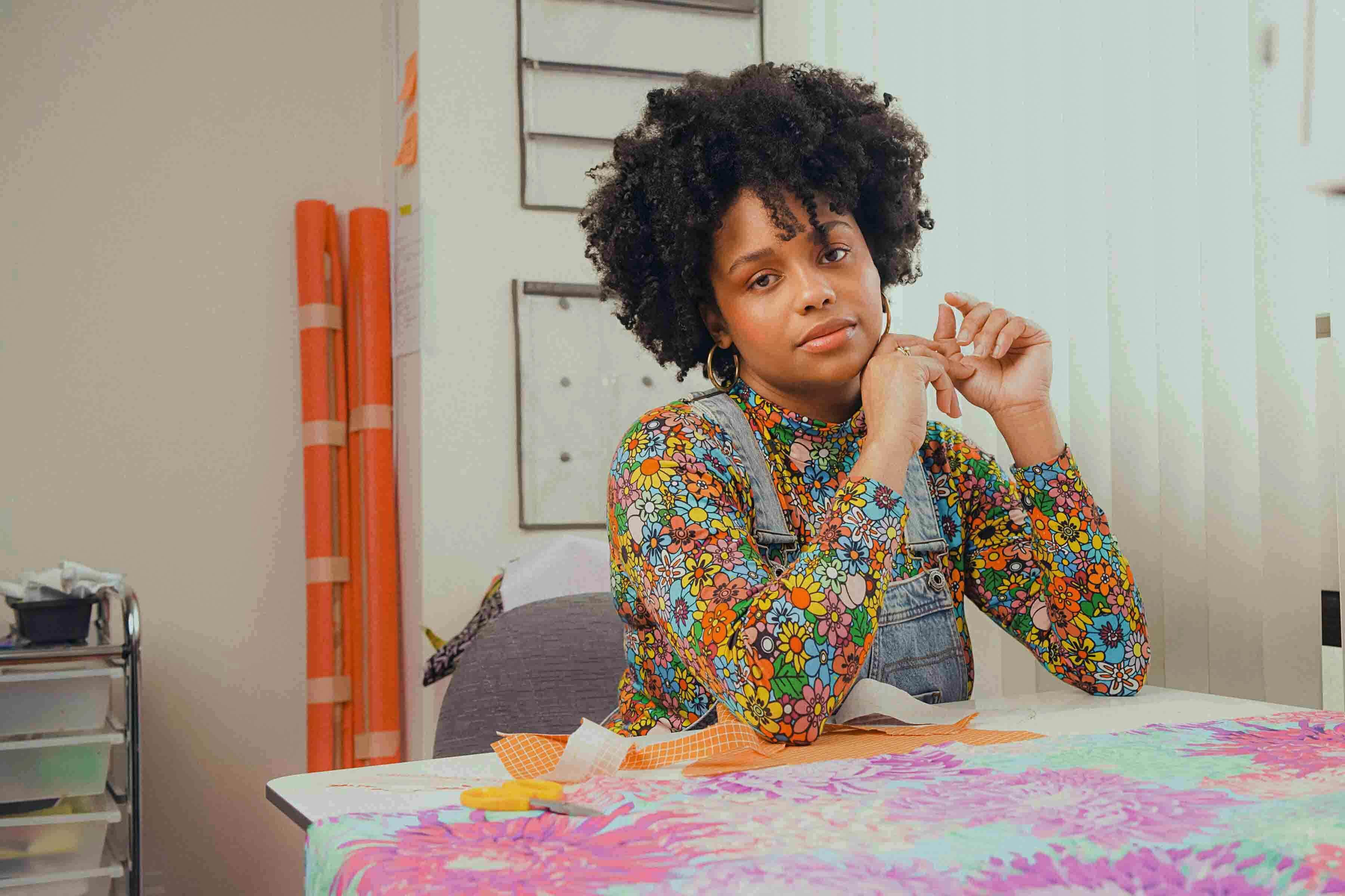 Gio Swaby sitting at a table with fabrics layed out in her studio