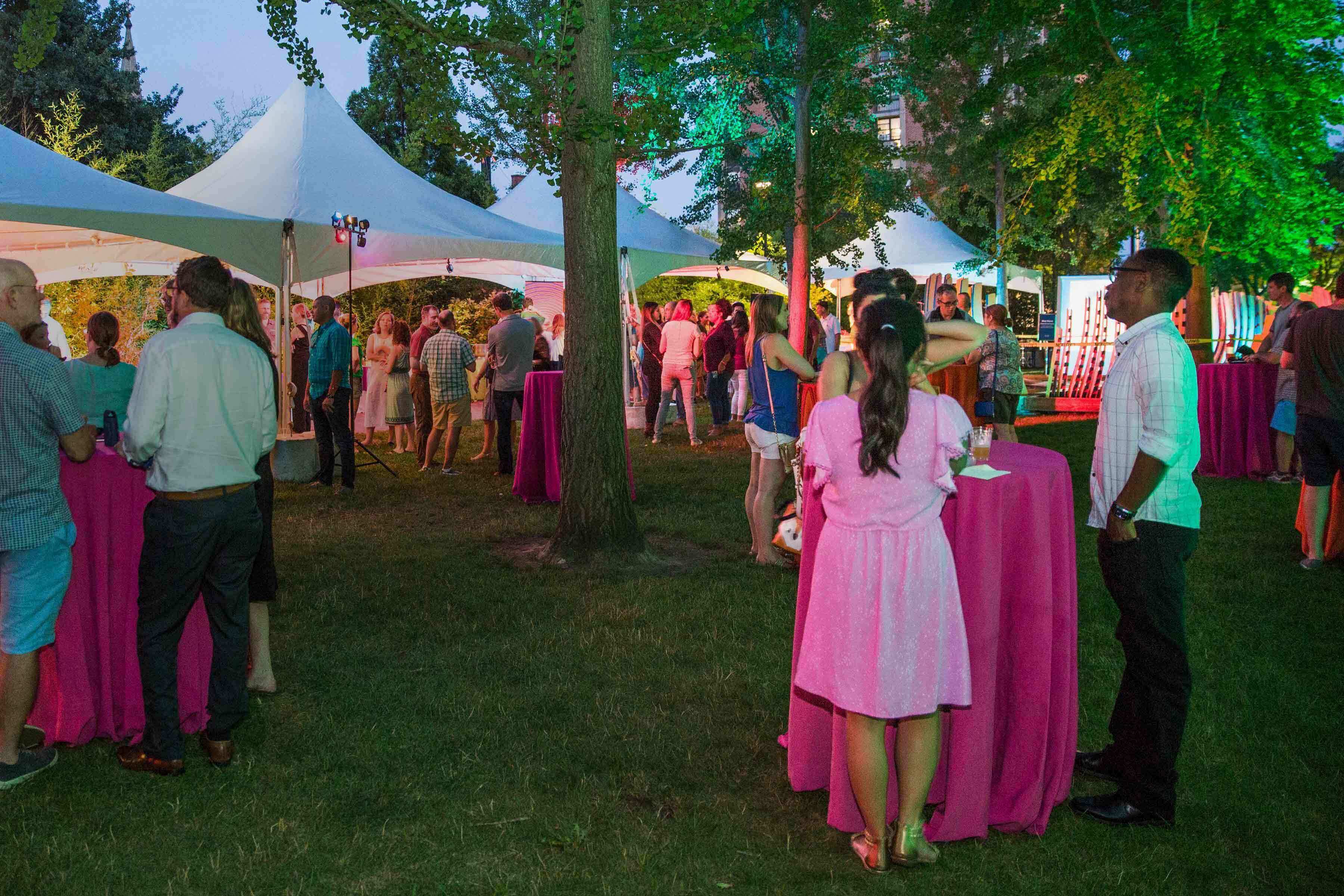 Several people standing and talking outside at white tablecloth covered tables with a large white tent in the background