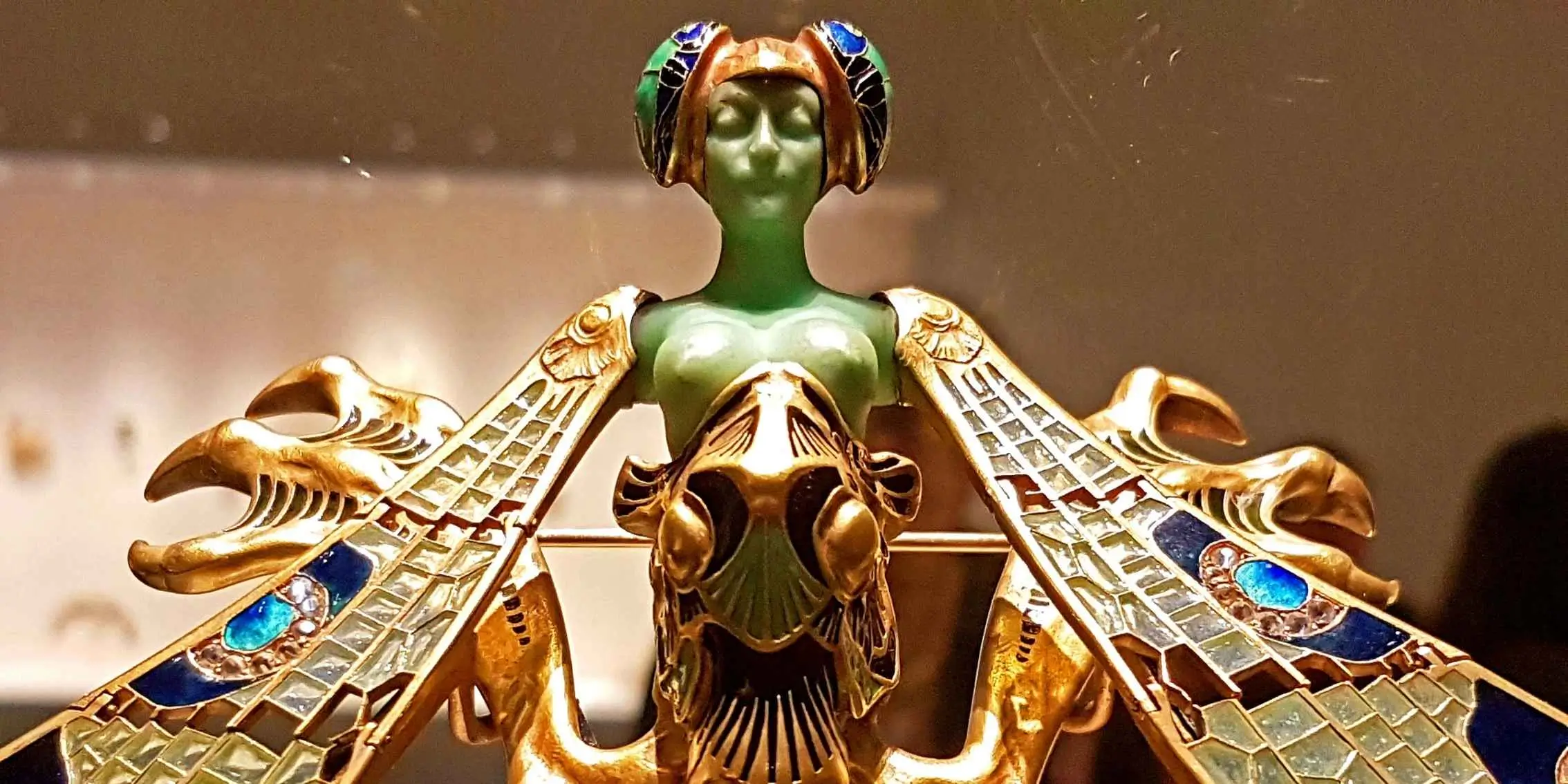 Art Nouveau decorative brooch featuring a green female figure with ornate
    gold and enamel insect-like wings