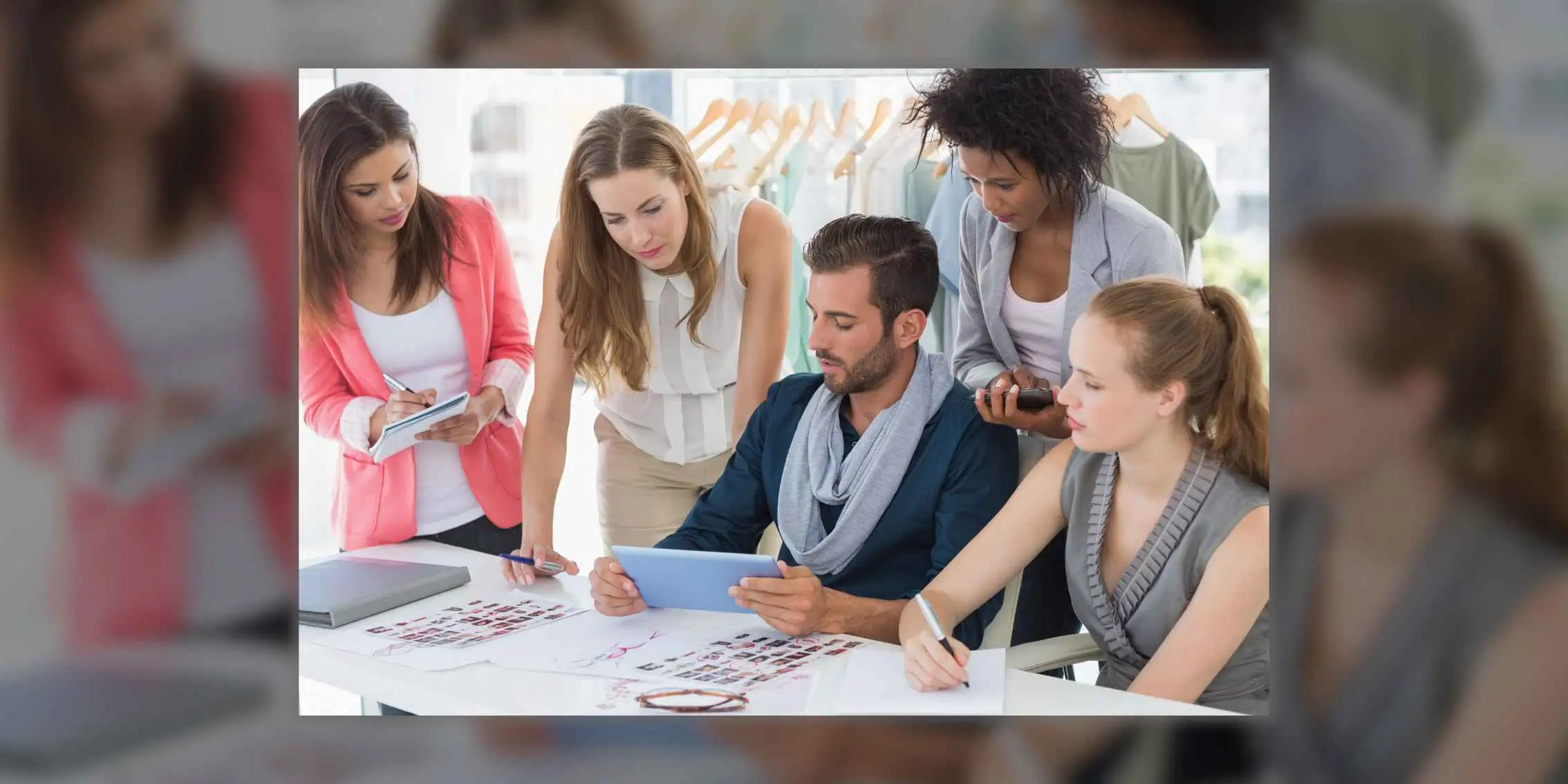 Title Fashion team collaborating around a table with sketches, digital tablet, and clothing rack in the background