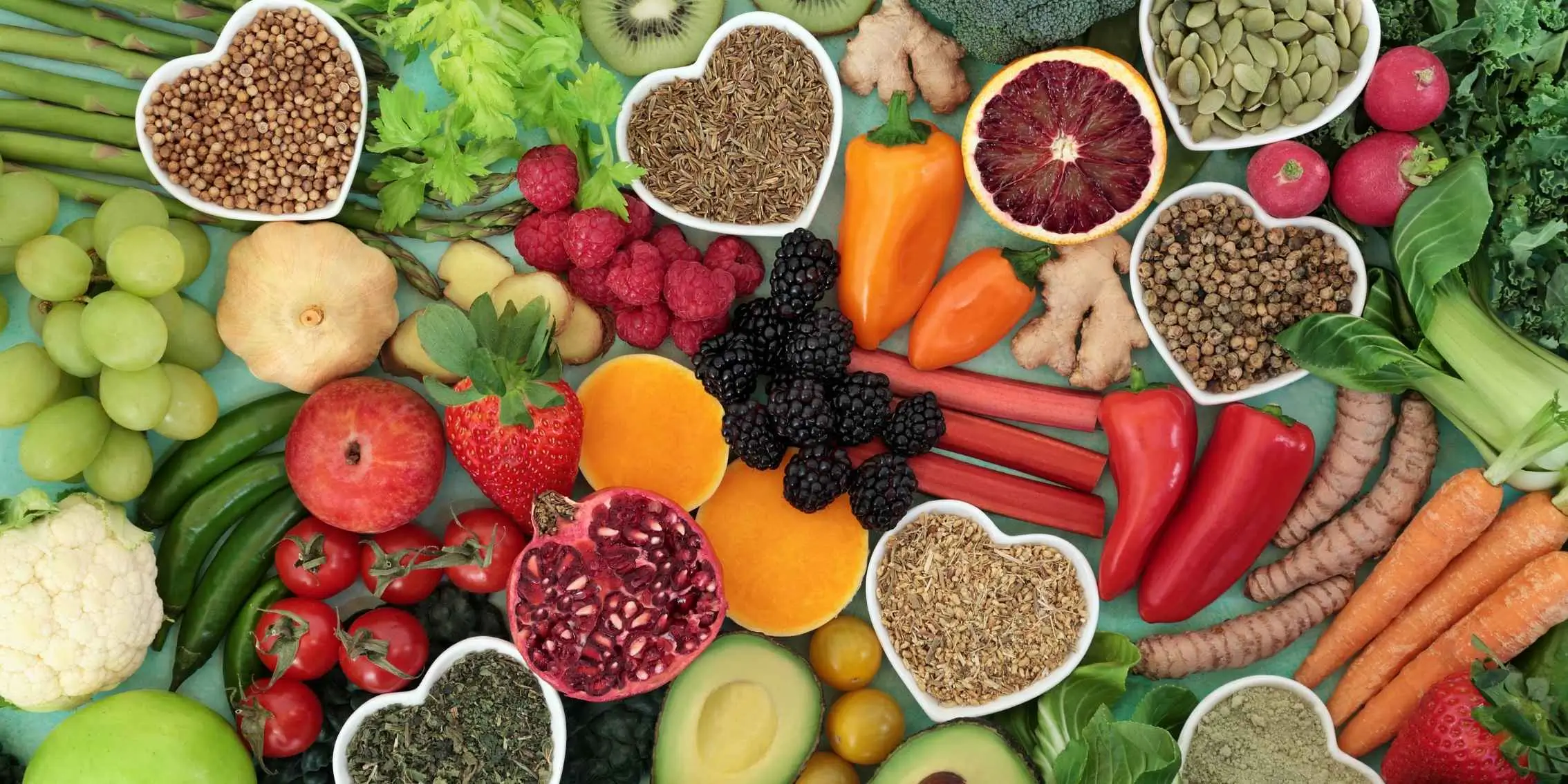 Colorful variety of fresh fruits, vegetables, seeds, herbs, and spices
        arranged on a flat surface with heart-shaped bowls