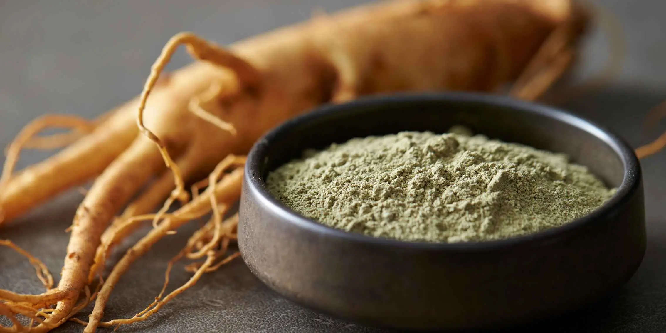 Ground ginseng root powder in a dark bowl with fresh ginseng roots in the
background