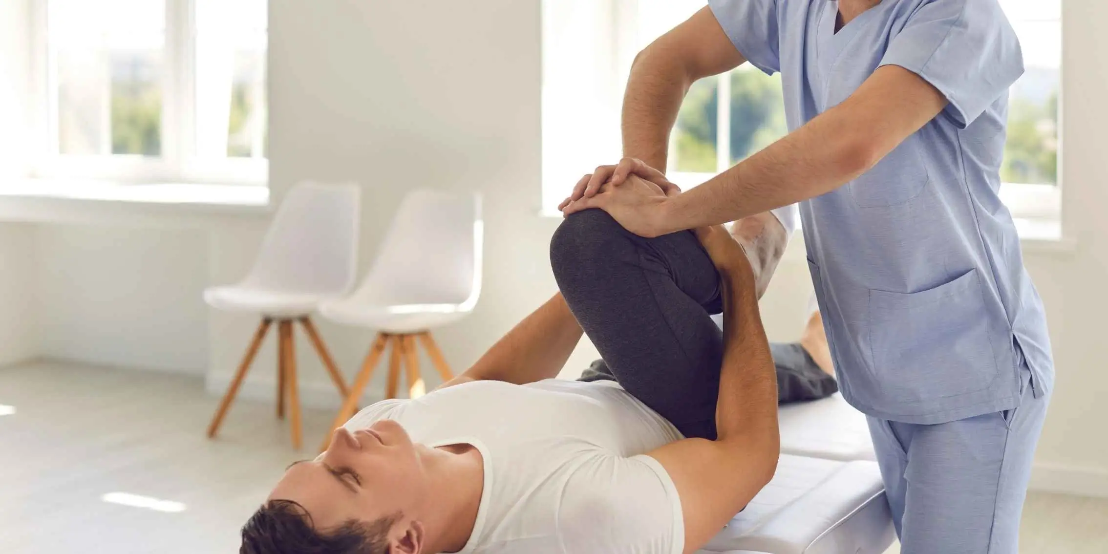 Physical therapist assisting a man with a leg stretch during rehabilitation
        in a bright clinical setting