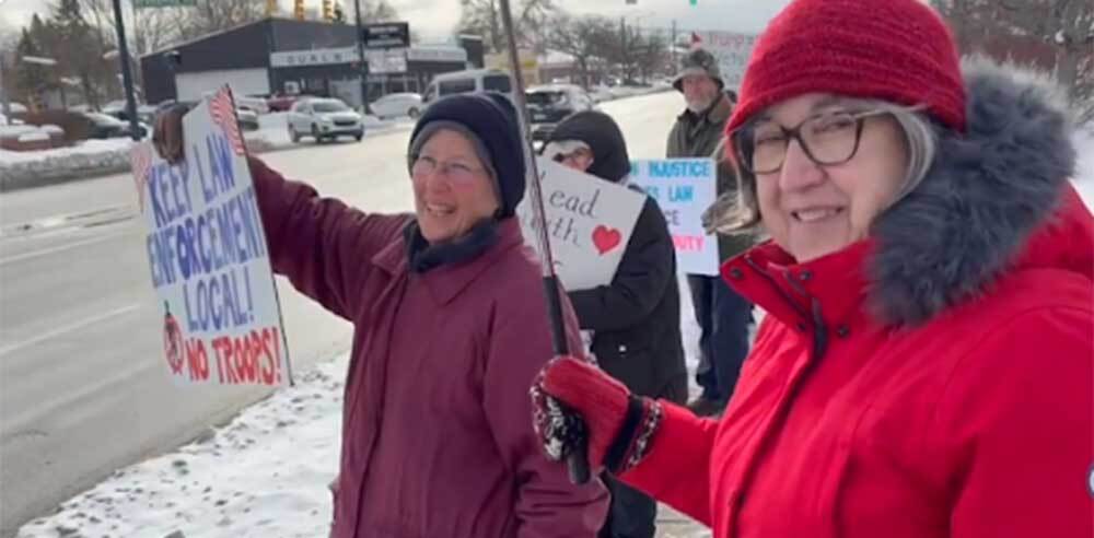 A group of Indivisibles stands on a street corner in the snow with signs and big smiles