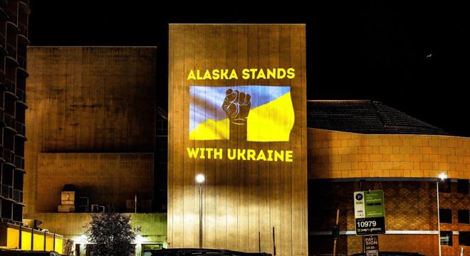 A Ukranian flag and the words ALASKA STANDS WITH UKRAINE projected in lights on a building in Anchorage, AK