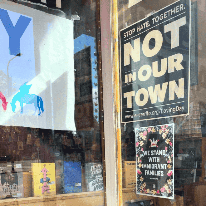 Photo: A sign that says WE STAND WITH IMMIGRANT FAMILIES, with a No Kings logo above the text, in the window of a bookstore in Oakland, CA