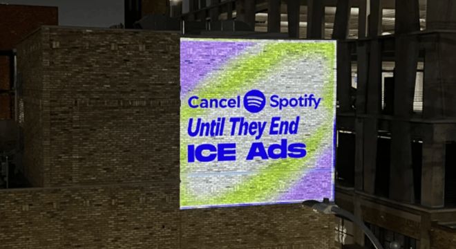 A building in downtown Los Angeles at night, with CANCEL SPOTIFY UNTIL THEY END ICE ADS projected onto it in lights
