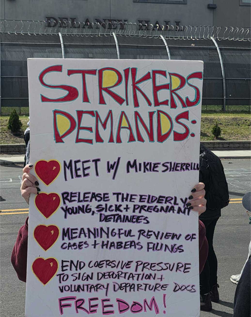 A protester outside Delaney Hall holding a sign that reads Strikers demands: Meet with Mikie Sherrill, release the elderly, young, sick and pregnant detainees, meaningful review of the cases and habeas findings, end coersive pressure to sign deportation and voluntarily departure docs. Freedom!
