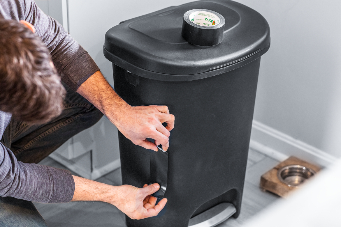 Man fixing crack in garbage can with black duct tape Man fixing crack in garbage can with black duct tape