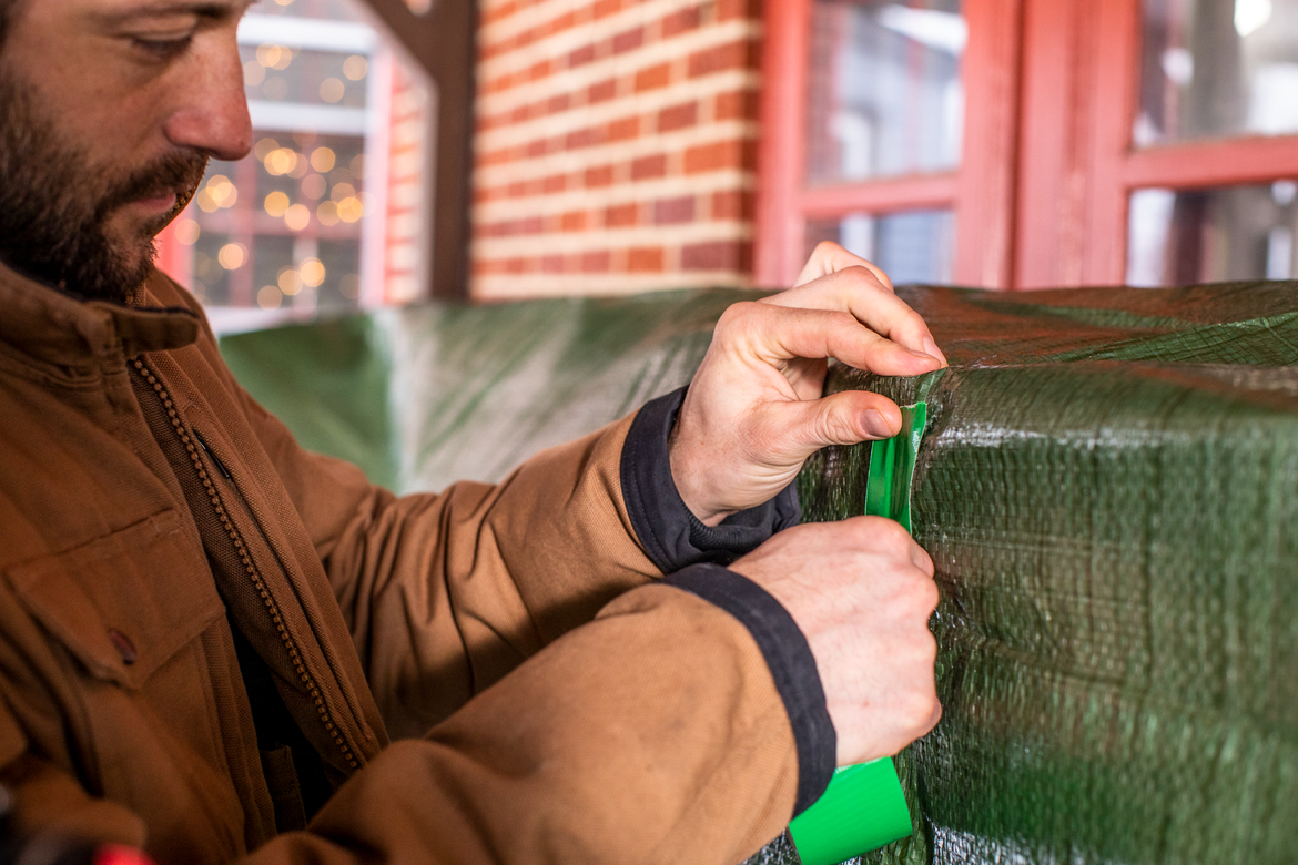 Man repairing green outdoor tarp with green duct tape Man repairing green outdoor tarp with green duct tape