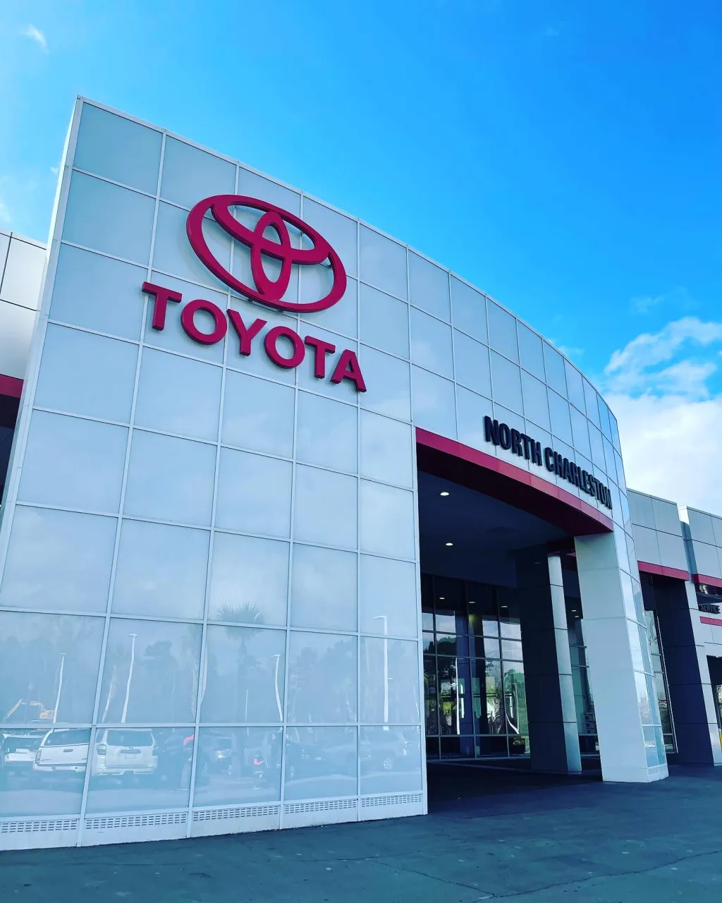 Toyota dealership exterior with illuminated brand signage across the facade and vehicle display area.