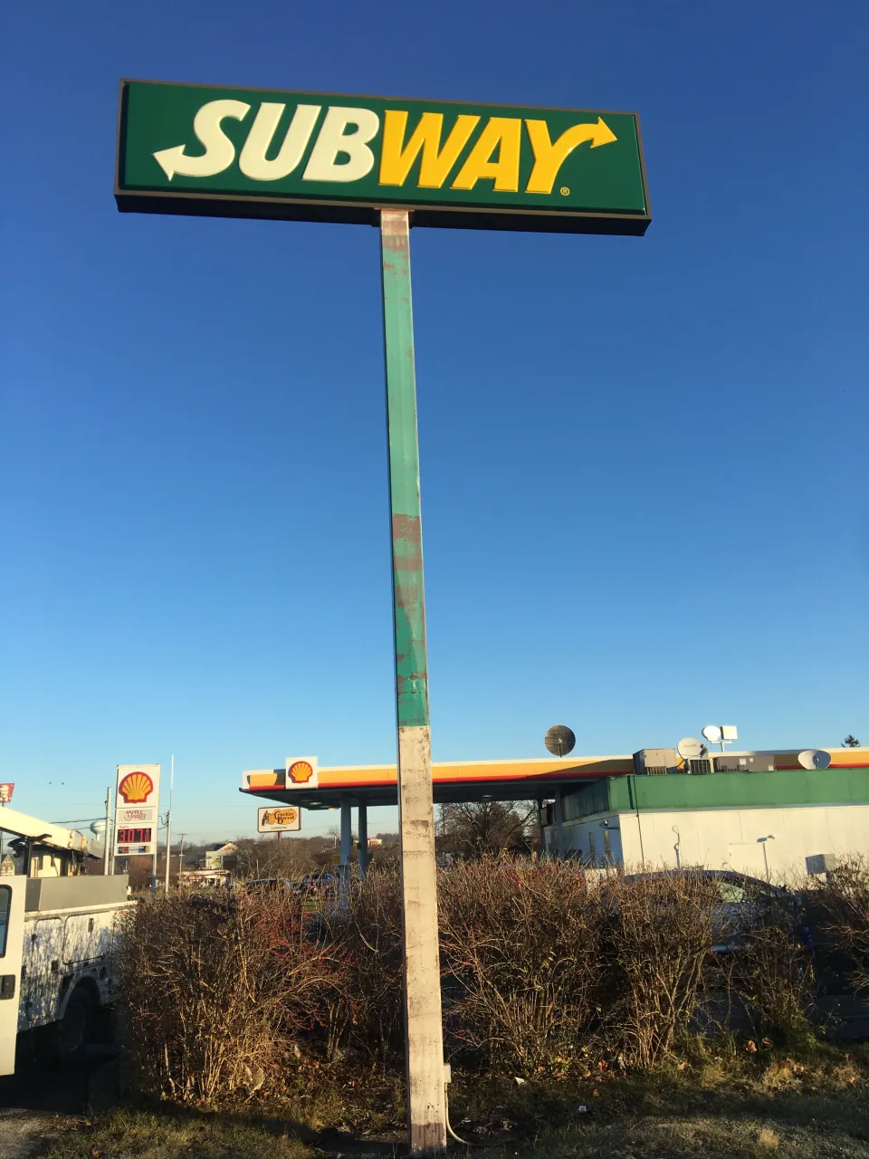 Very tall pole‑mounted Subway restaurant sign rising above the surrounding trees.