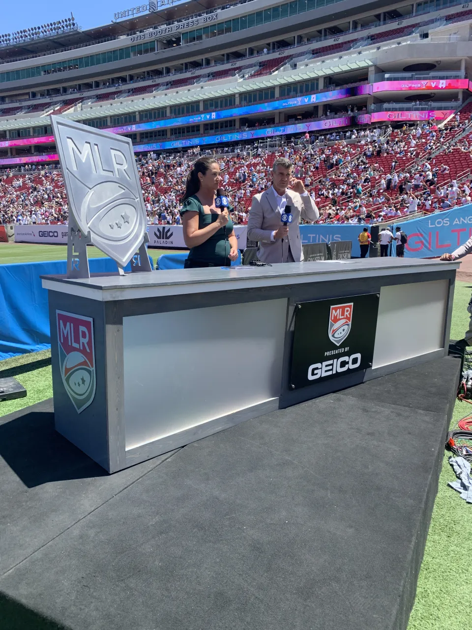 Completed black Major League Rugby sign with logo and Geico sponsor panel mounted across the front of a custom broadcast desk.
