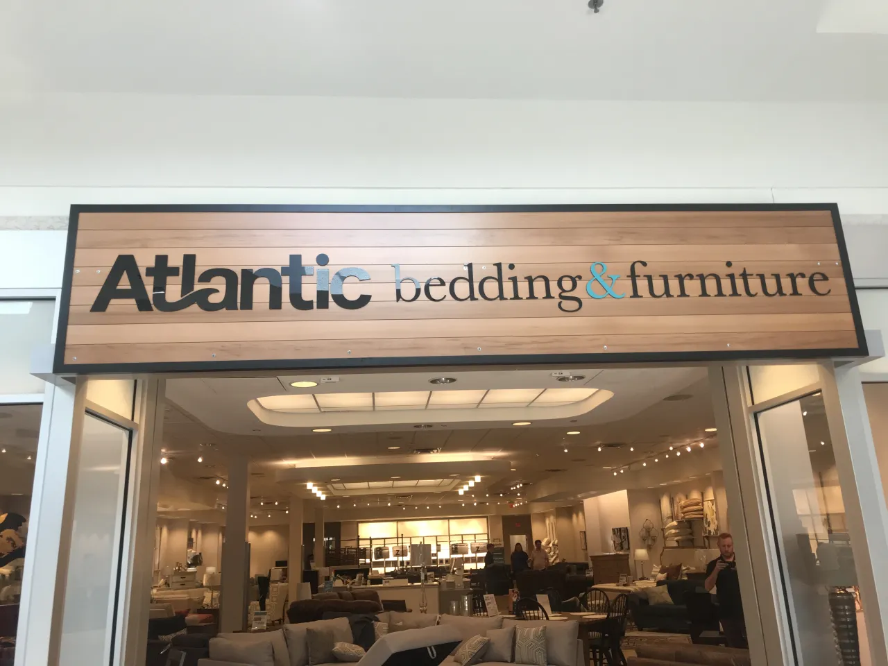 Black Atlantic Bedding and Furniture storefront sign mounted above the entrance on a warm wooden slat background, lit evenly across the cabinet.