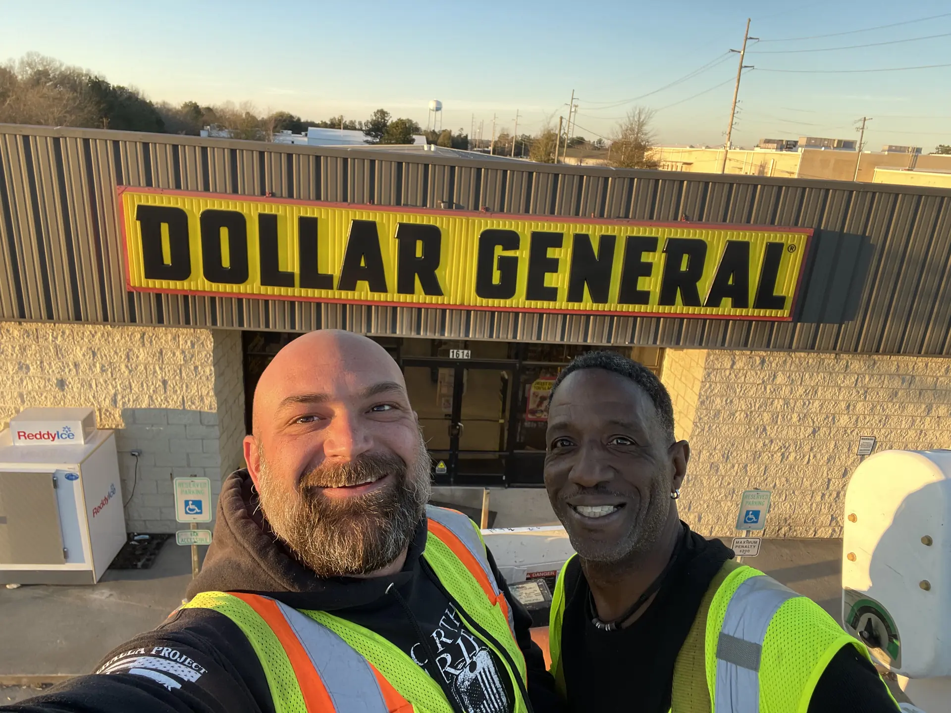 Dollar General storefront sign with illuminated cabinet mounted above the entrance, with the owner standing to the left and the installer to the right in front of the building.