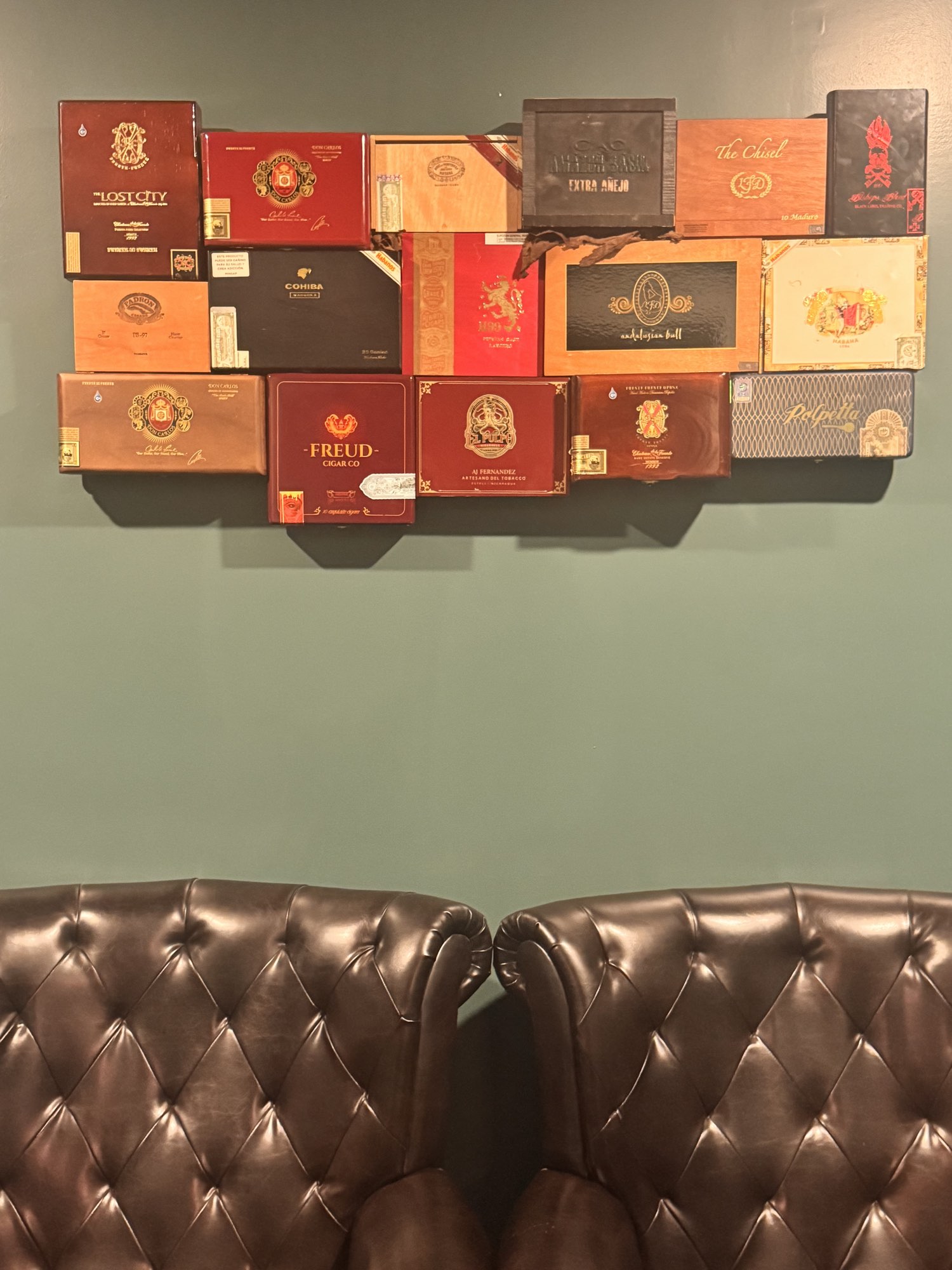 A wall of collected boxes above two tufted leather armchairs