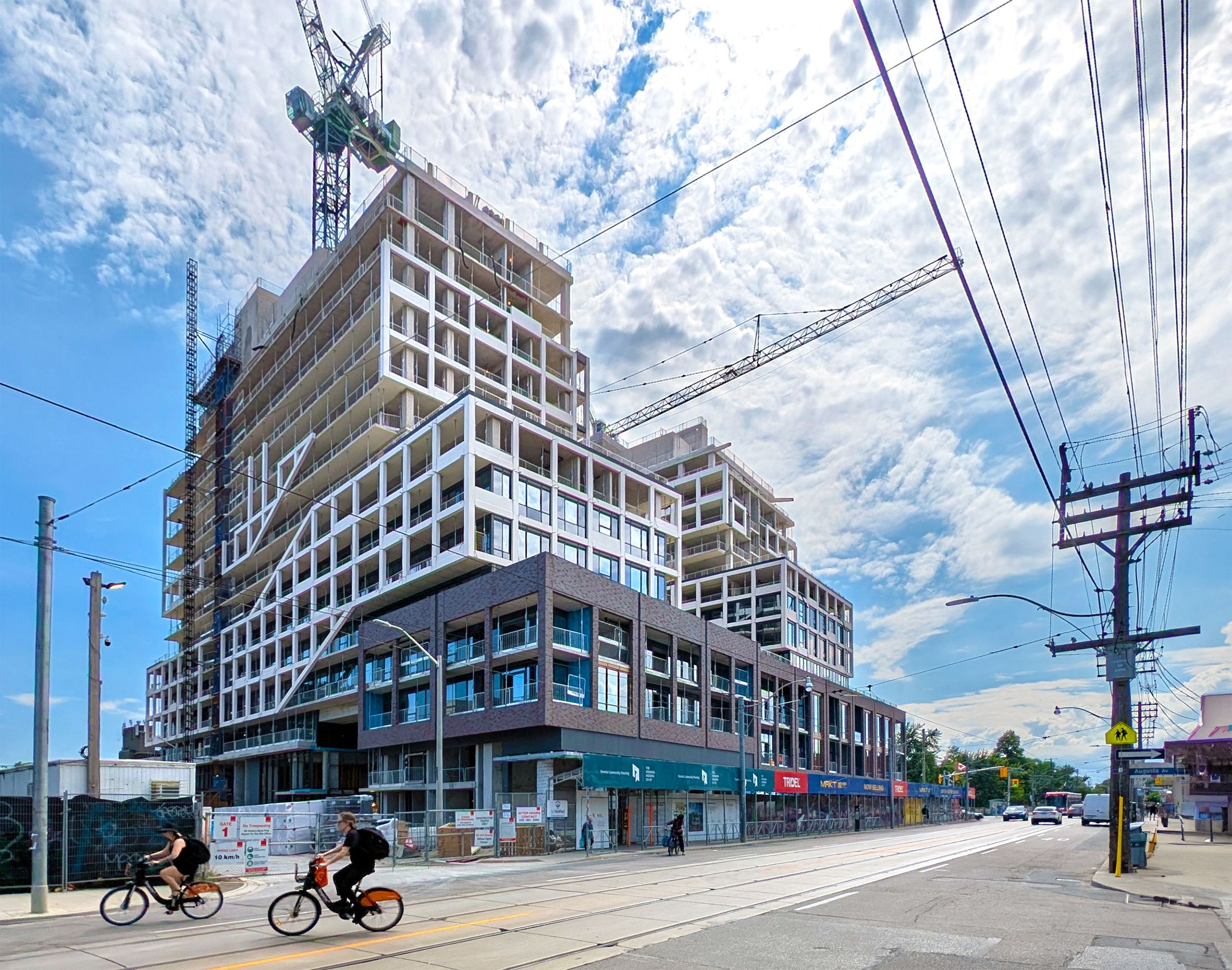 Mixed-use development under construction featuring a stepped architectural design with retail at street level and residential units above, located along a transit corridor.