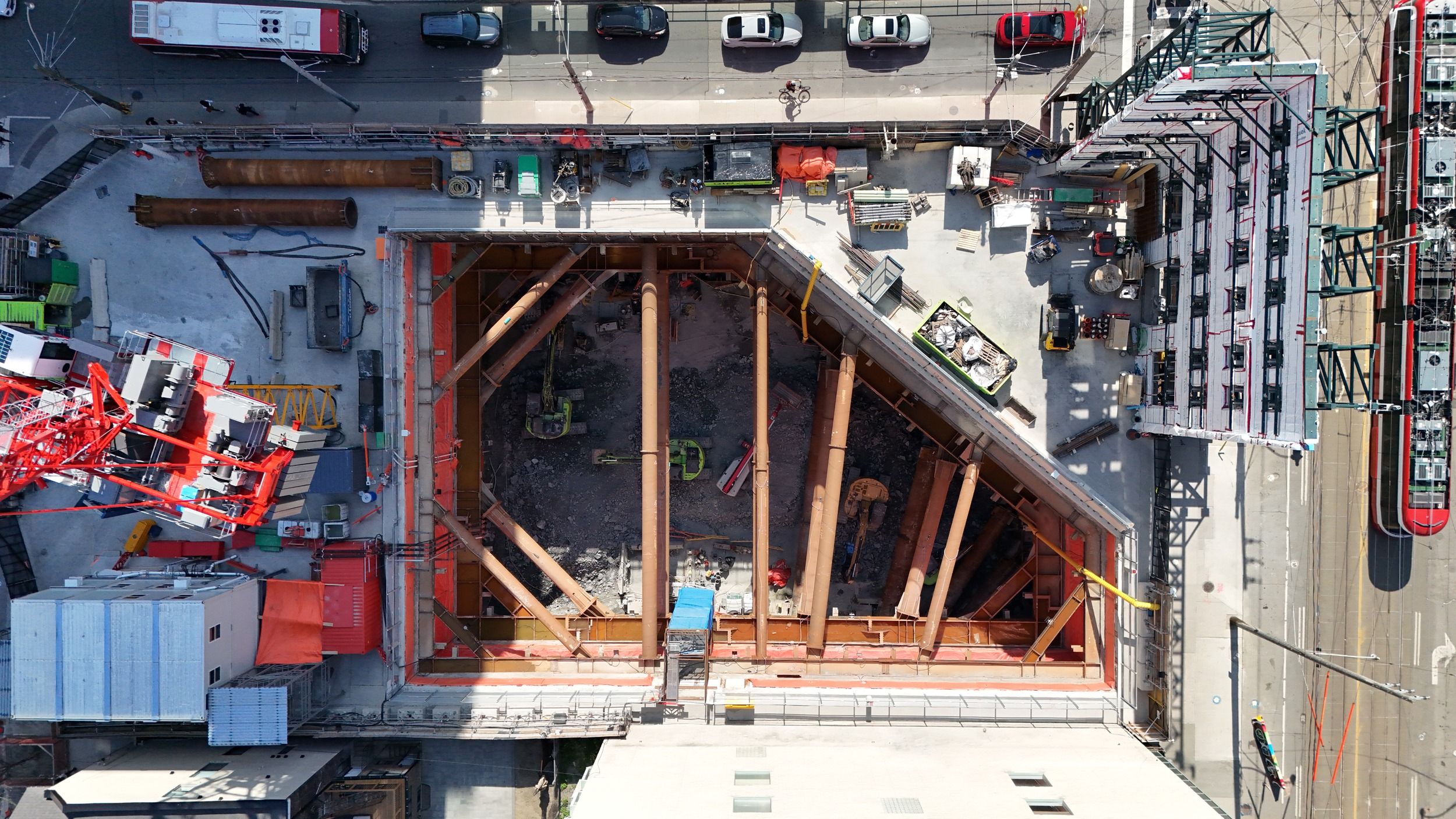 Aerial view of active subway construction site showing foundation work with temporary support beams and surrounding construction equipment.
