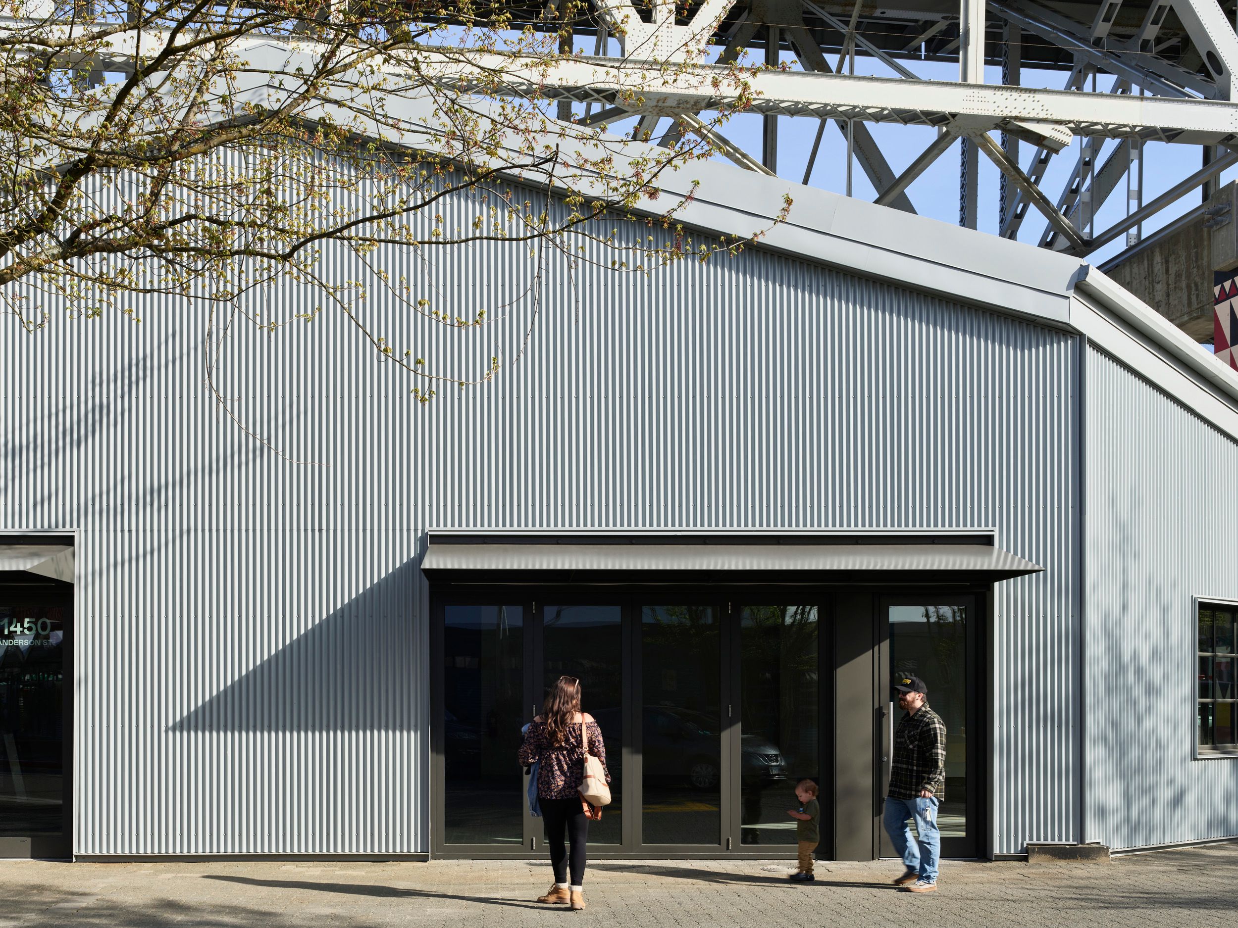 Modern industrial-style building entrance with corrugated metal exterior and glass doorway under structural steel framework.