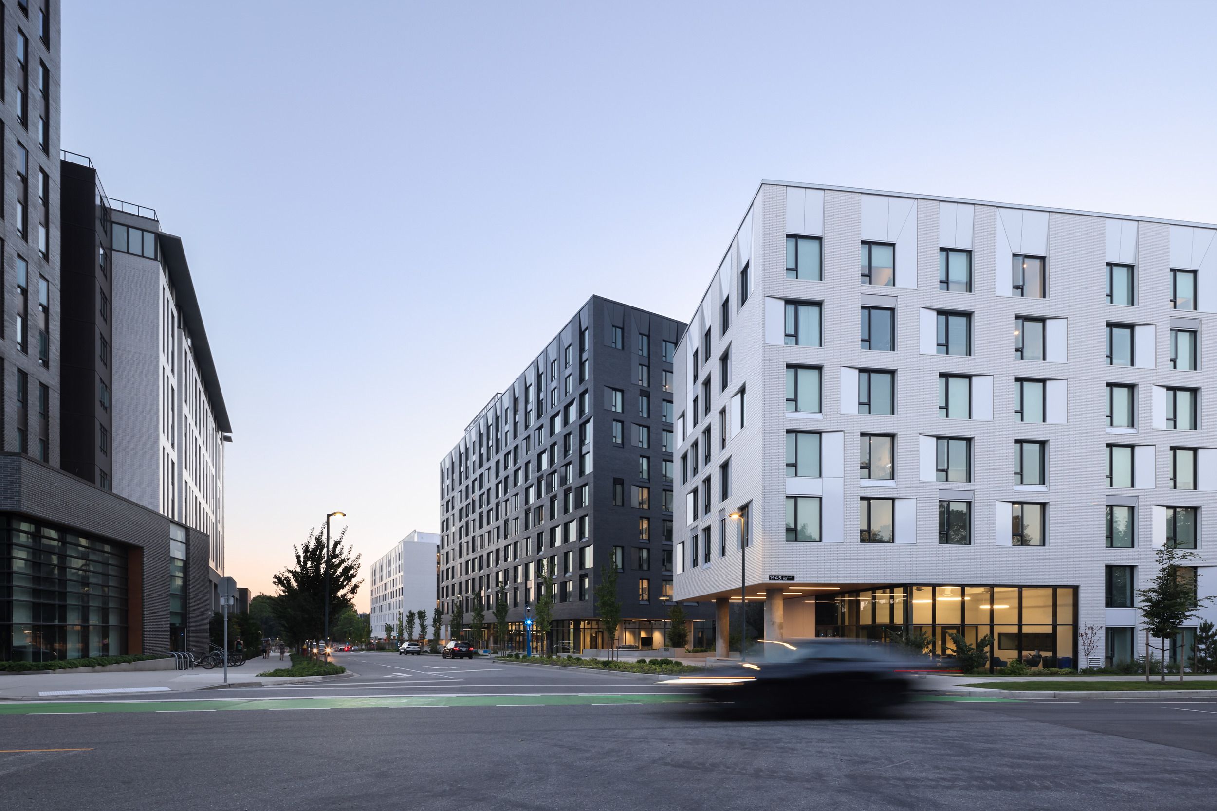 Modern student residence development featuring multiple mid-rise apartment buildings with ground-floor retail space along a wide street corner.