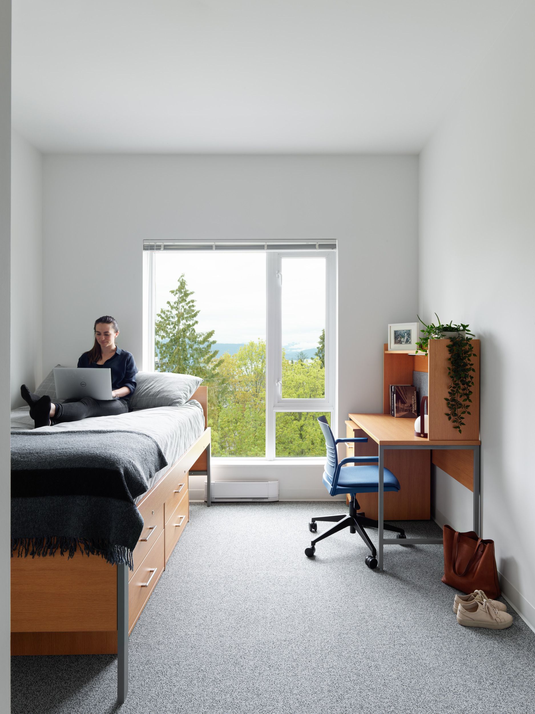 Modern open-concept student residence interior featuring a kitchen breakfast bar, living area, and large windows overlooking urban buildings.