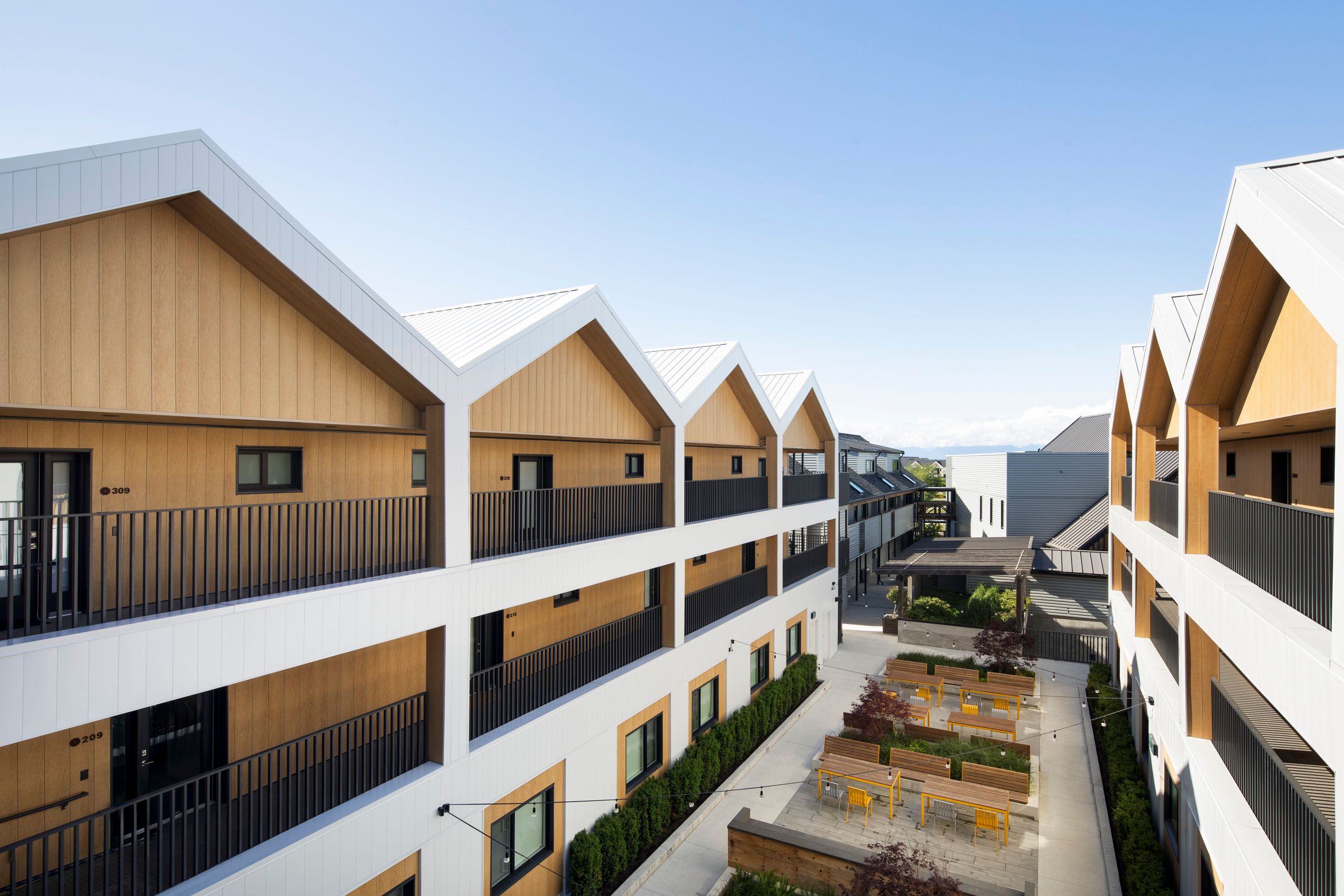Modern multi-unit residential complex featuring distinctive peaked rooflines and a central courtyard with outdoor seating areas.