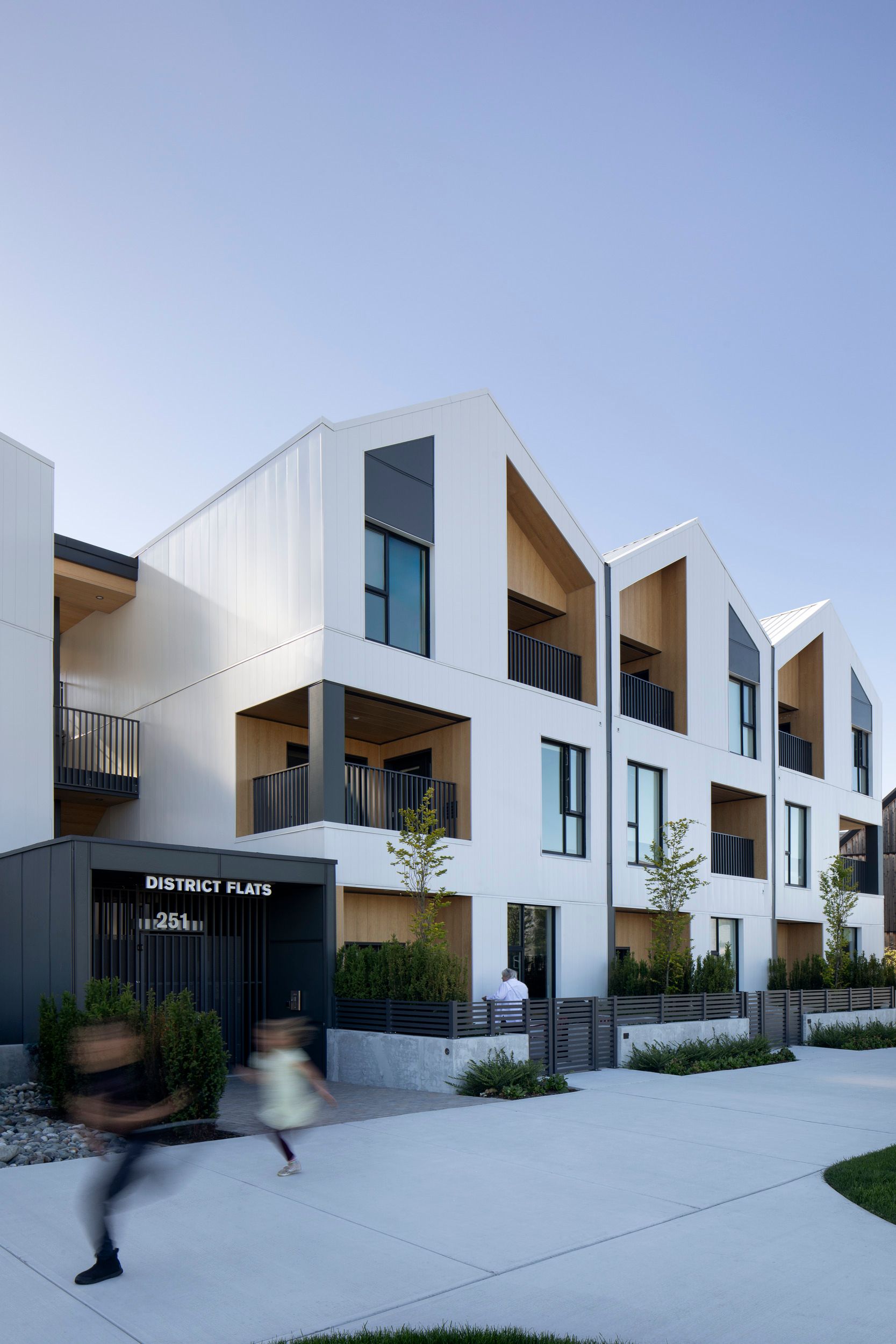 Modern multi-unit residential development called "District Flats" featuring white angular architecture with private balconies and a contemporary minimalist design.