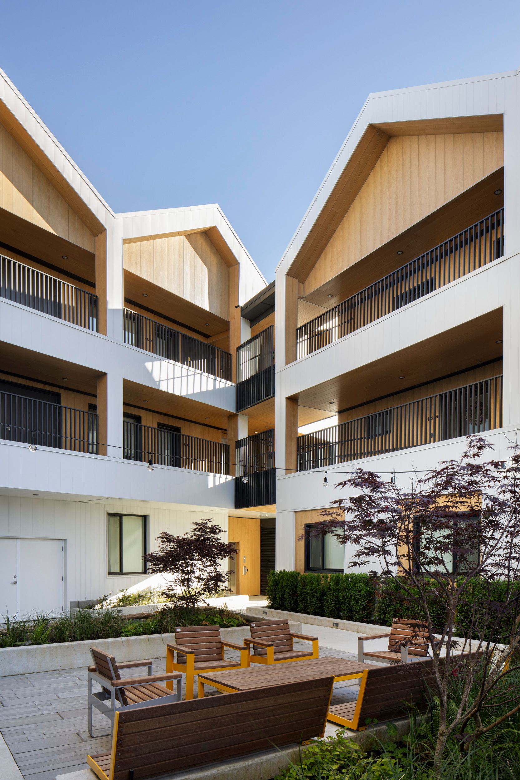 Modern multi-story residential building featuring a central courtyard with outdoor seating and landscaped garden areas.