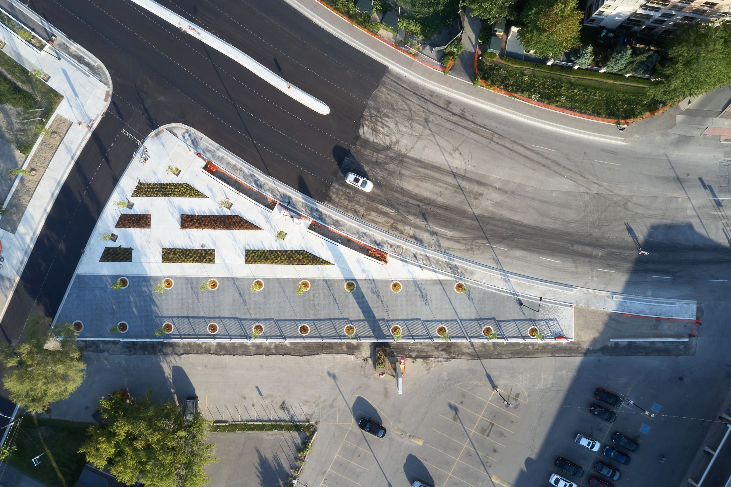 Aerial view of a triangular plaza featuring landscaped garden beds and a row of street trees along its perimeter.