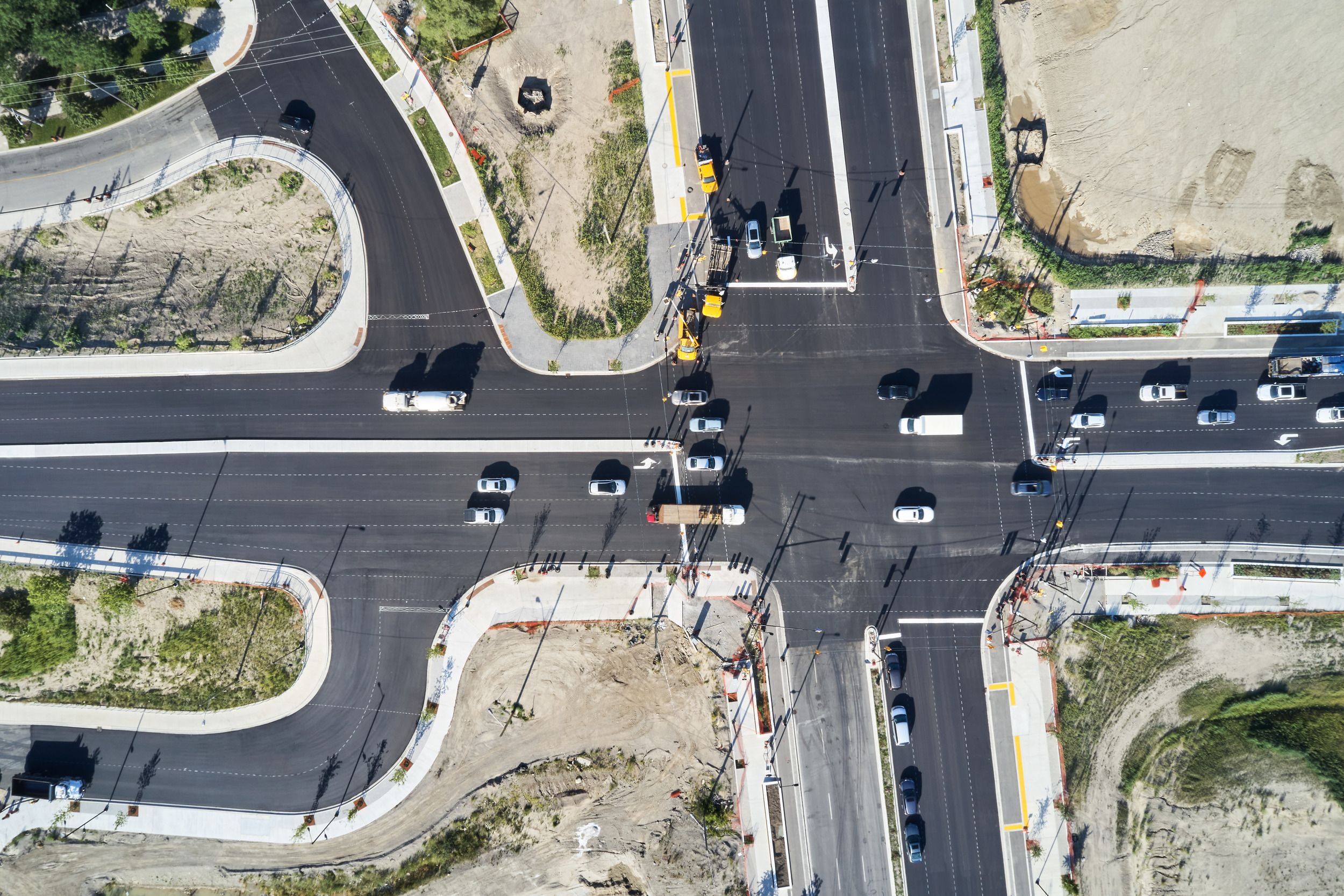 Aerial view of a four-way intersection with traffic signals and ongoing construction work on surrounding undeveloped lots.
