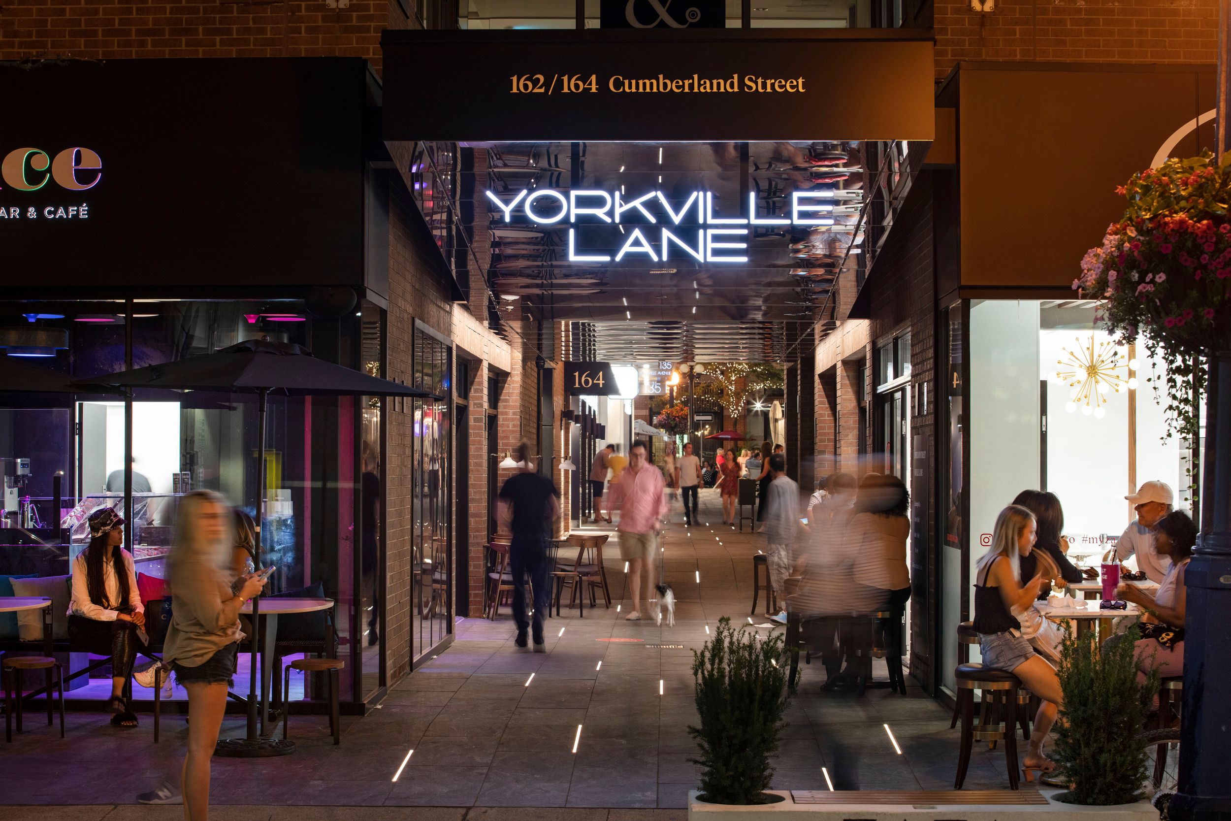 Yorkville Lane entrance and retail corridor at night, showing illuminated signage and outdoor dining areas with patrons.