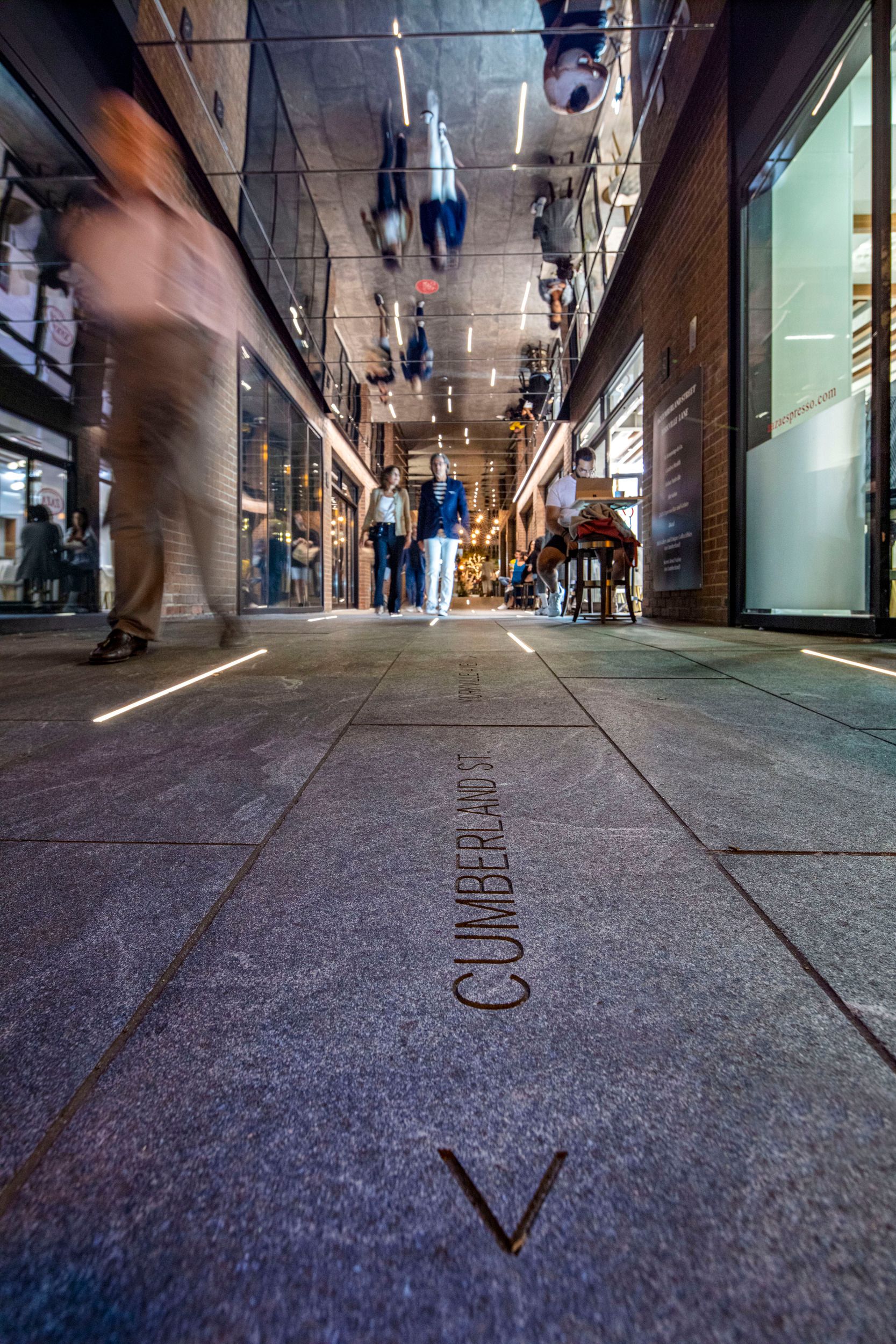 Indoor shopping corridor with "Cumberland St" engraved in the floor, featuring modern lighting and retail storefronts on both sides.