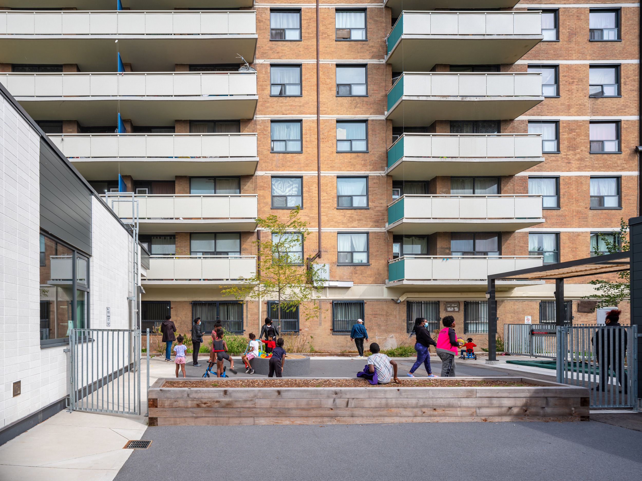 Modern apartment building courtyard with raised wooden planters and communal gathering space in an urban residential setting.