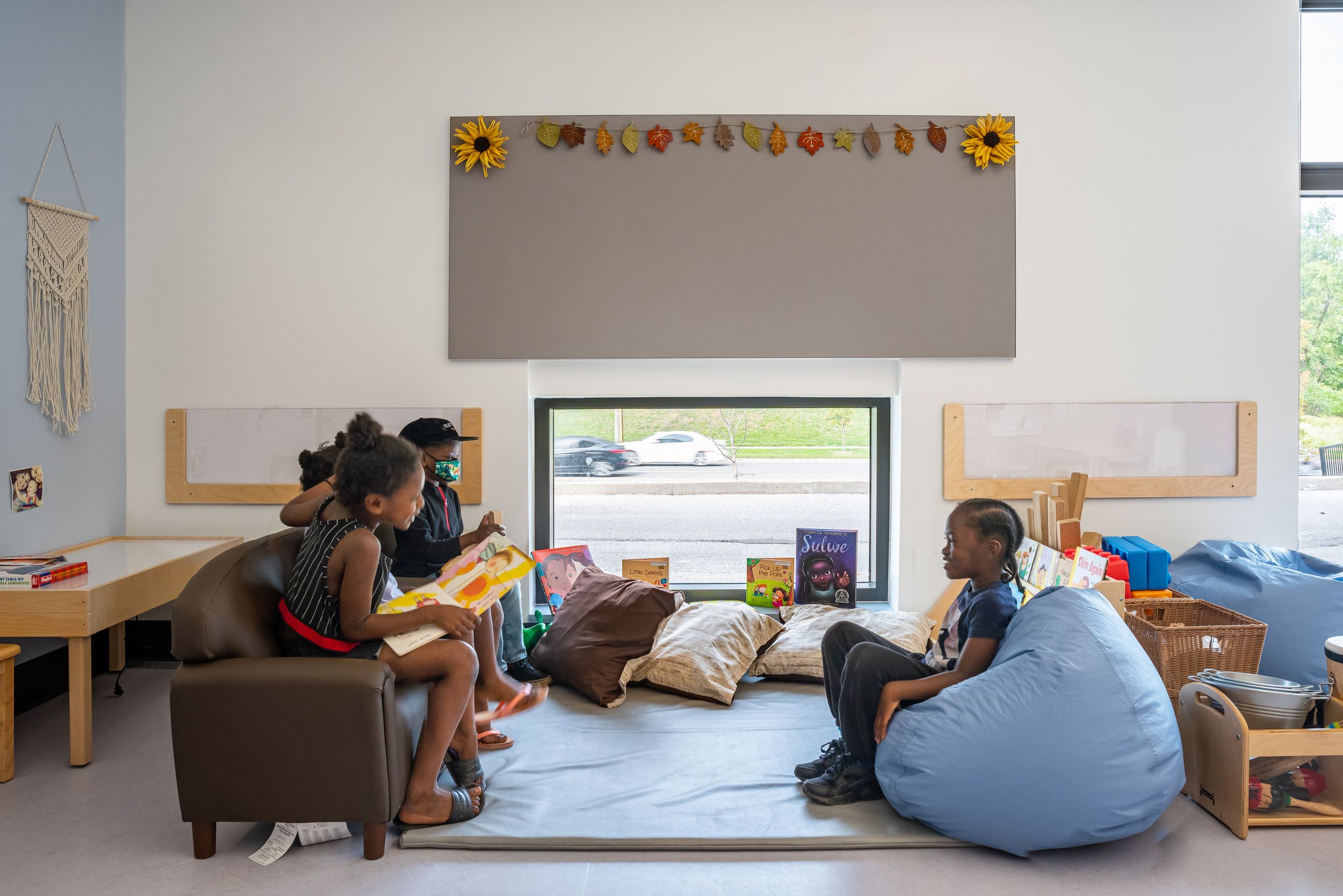 Cozy reading nook in a classroom featuring comfortable seating, pillows, and fall-themed decorations above the window.