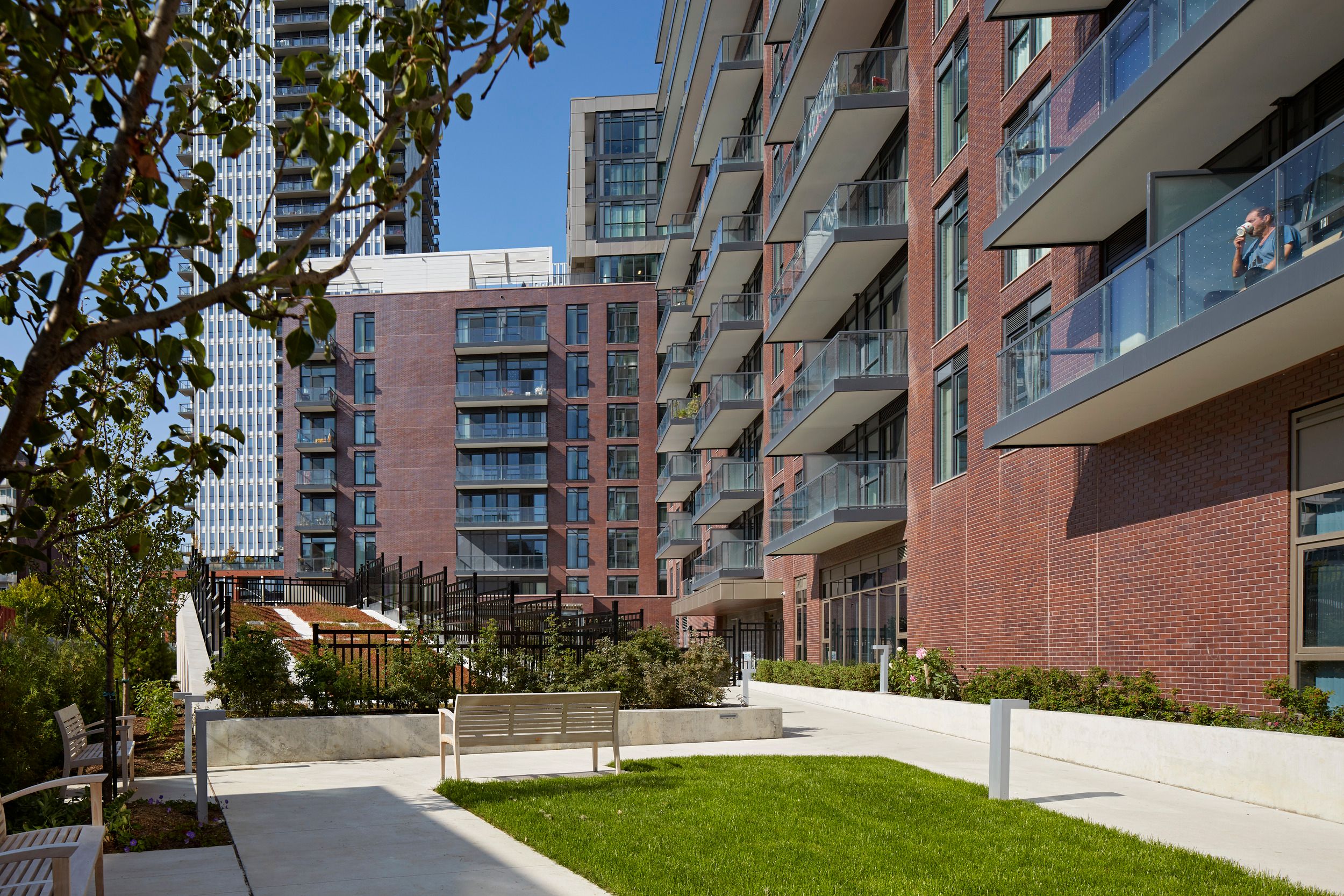 Complejo de apartamentos moderno con fachadas de ladrillo, balcones de vidrio y un patio ajardinado con áreas de descanso.