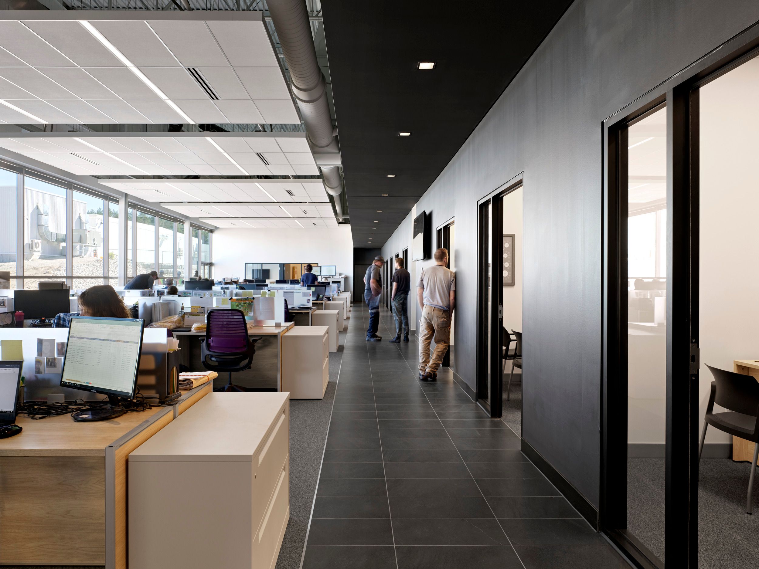 Modern open-plan office space featuring workstations, private meeting rooms, and floor-to-ceiling windows offering city views.