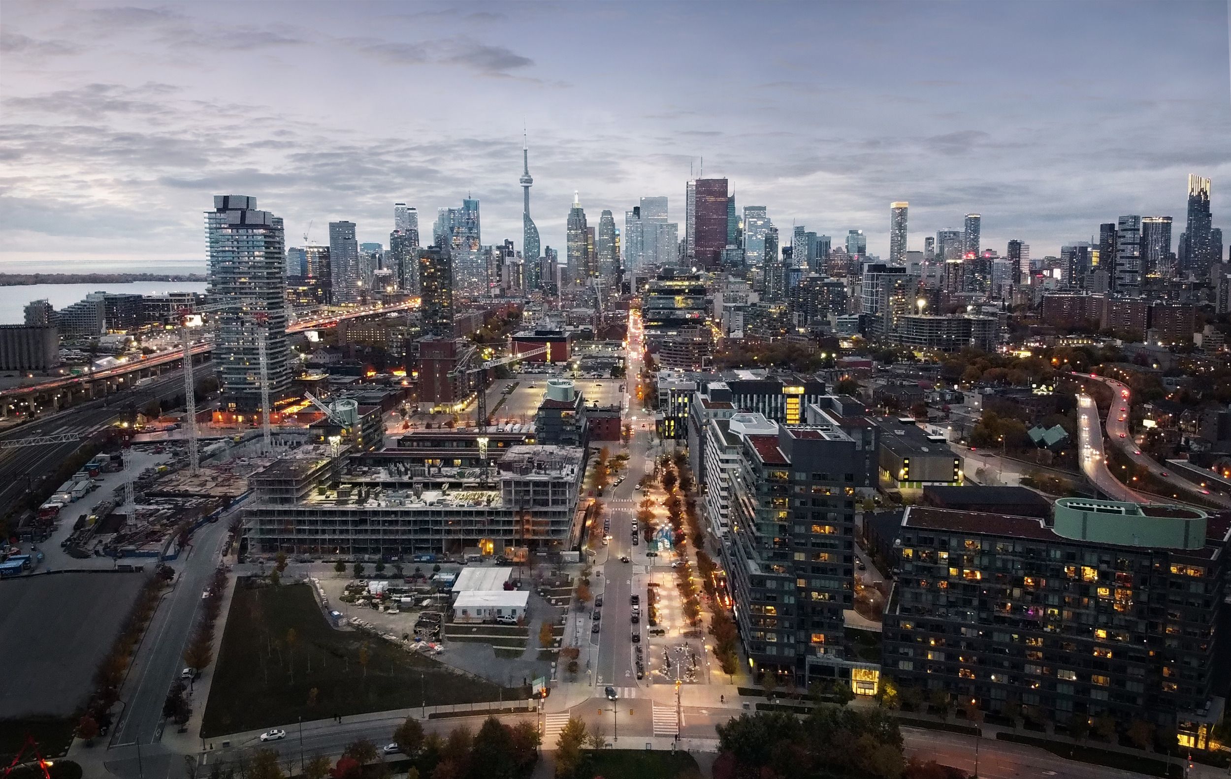 Toronto skyline at dusk showing downtown core with CN Tower, illuminated streets, and urban development extending towards the waterfront.