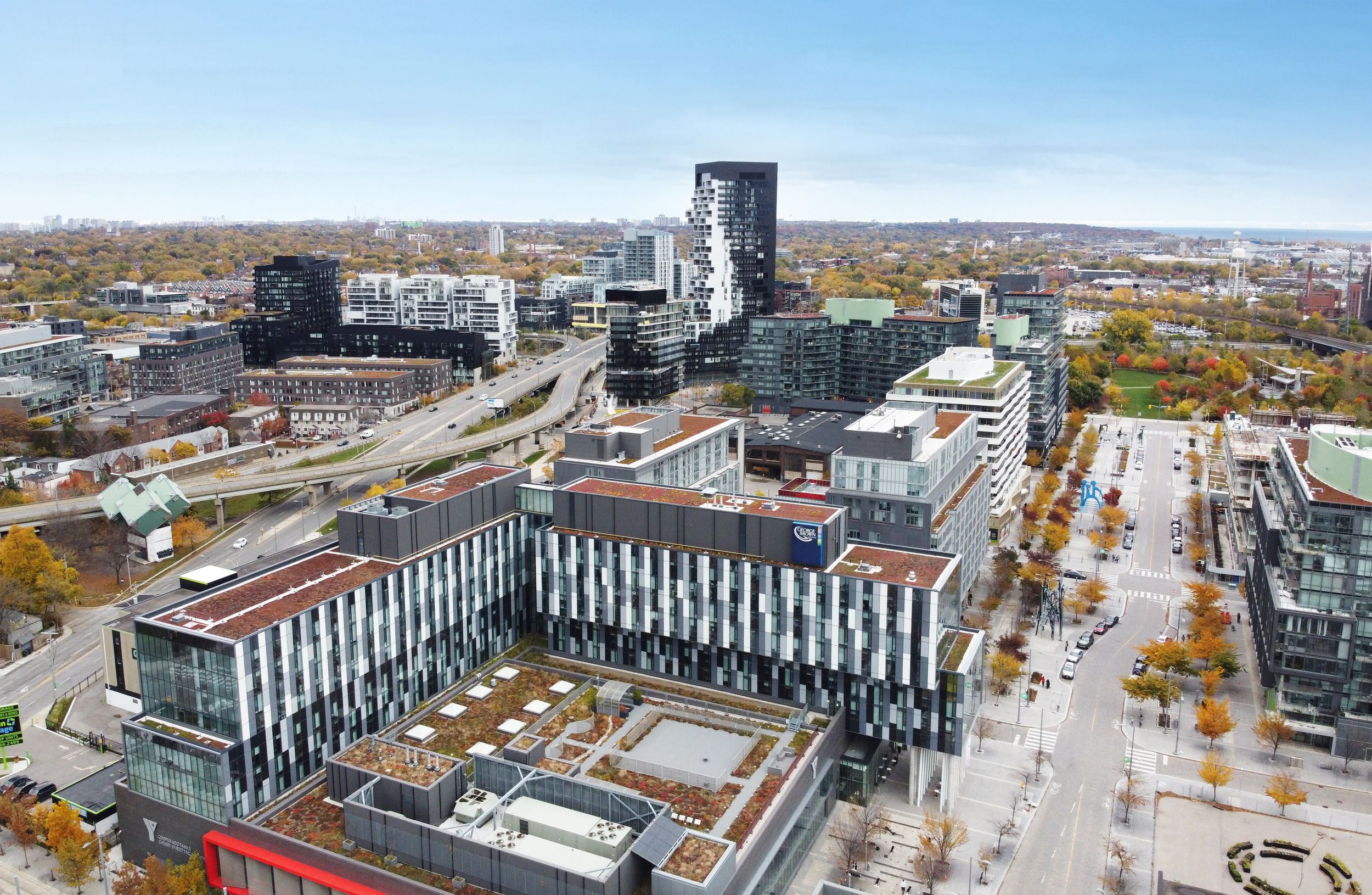 Aerial view of a modern urban development showing commercial buildings, residential towers, and tree-lined streets during autumn.