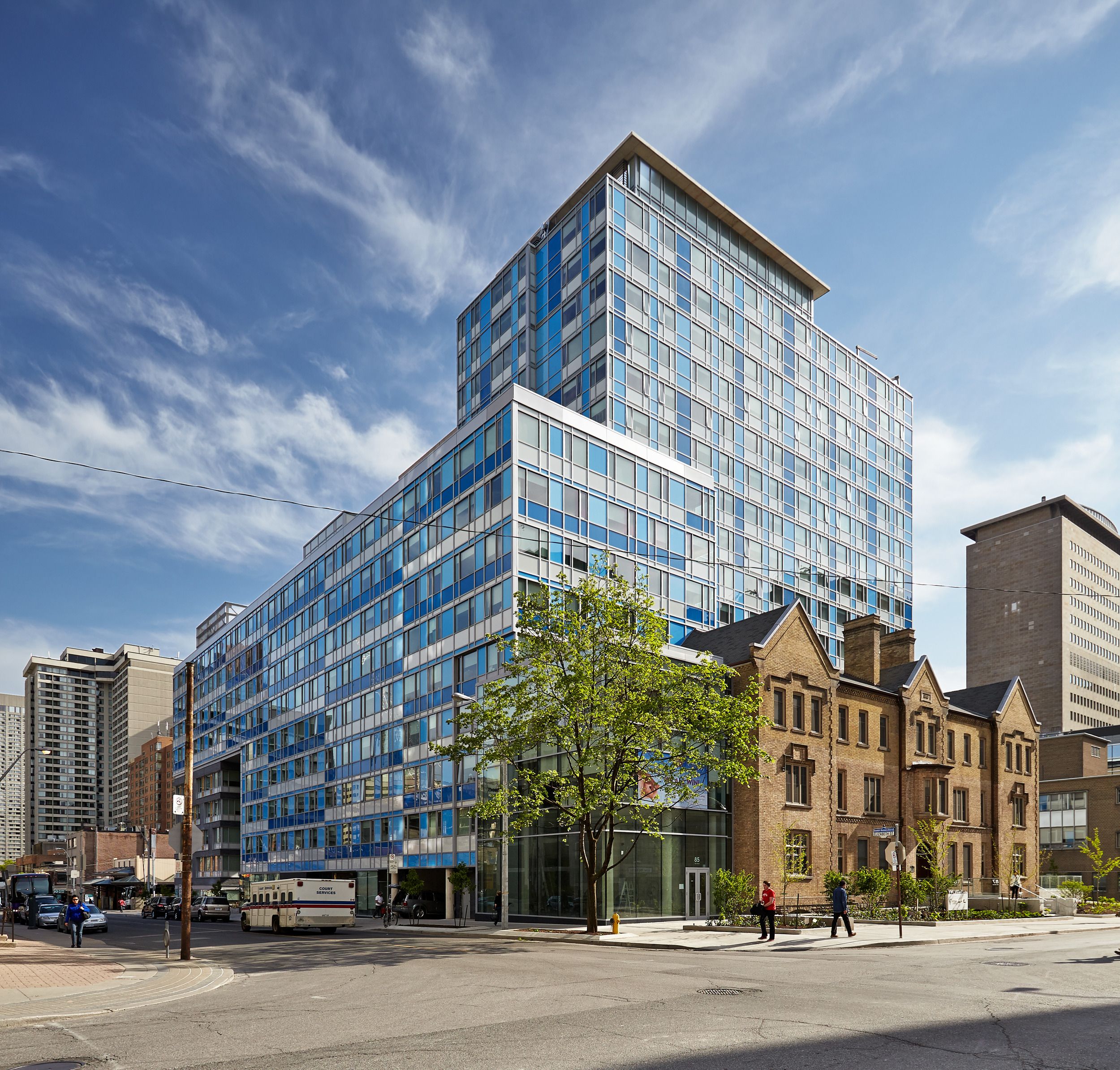 Modern glass high-rise apartment building contrasting with heritage building on an urban street corner.
