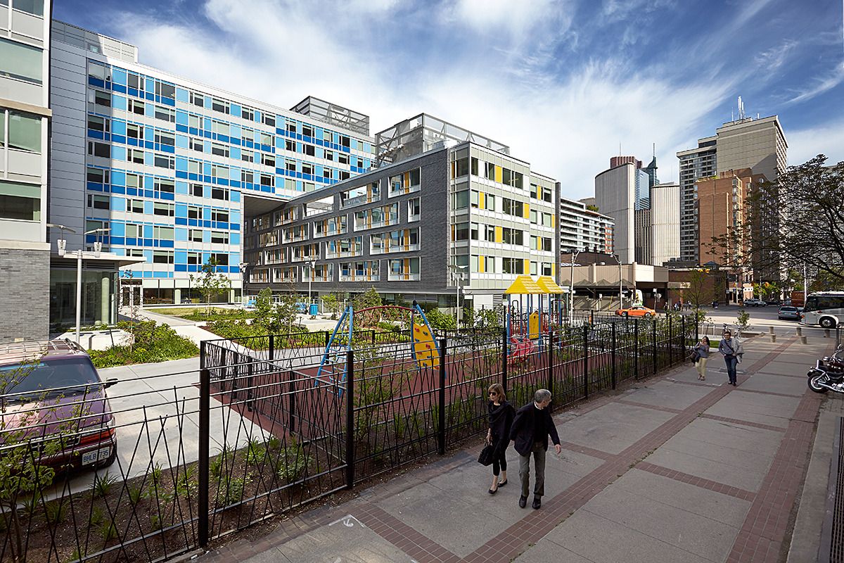 Modern urban residential development featuring colorful apartment buildings, a children's playground, and pedestrian walkway against a city skyline.