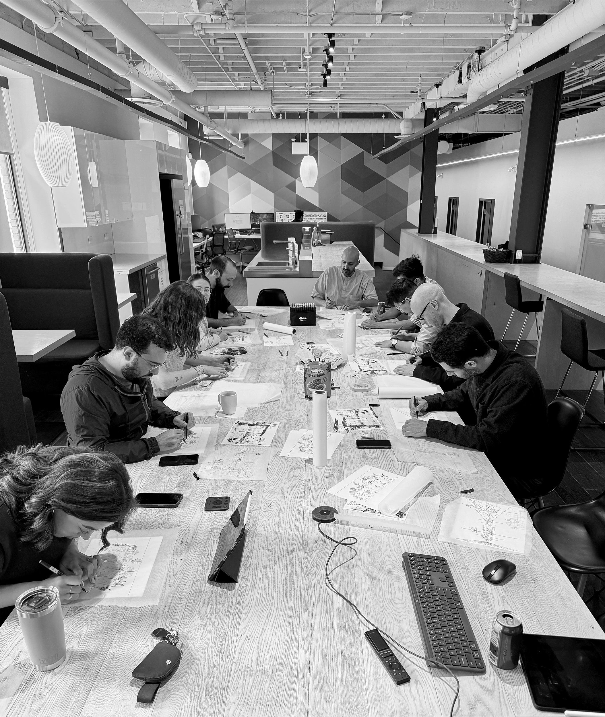Modern open office space featuring designers sketching together at a long communal table.