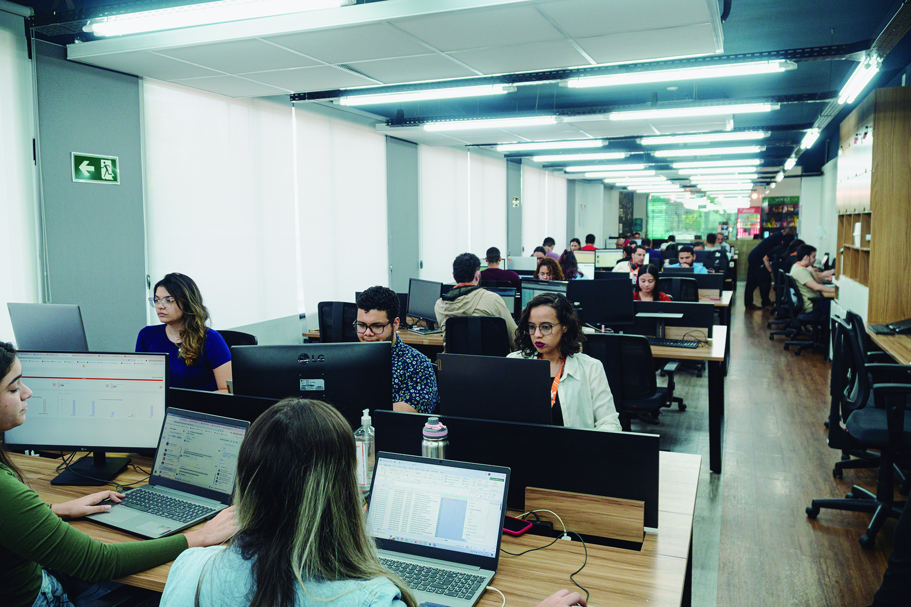 Ambiente corporativo amplo com várias pessoas trabalhando em estações de trabalho.