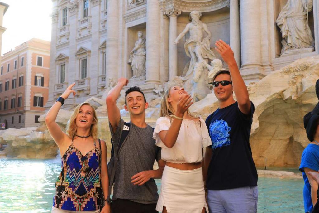 Teenage travelers throw coin in Trevi fountain during summer youth travel program in Rome
